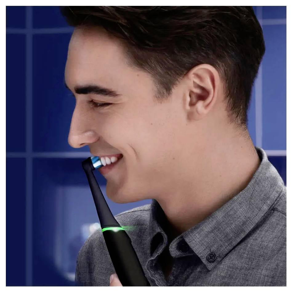 Een persoon glimlacht terwijl hij of zij een elektrische tandenborstel gebruikt in een badkamer, waarbij de nadruk wordt gelegd op mondhygiëne en moderne verzorgingsgewoonten.