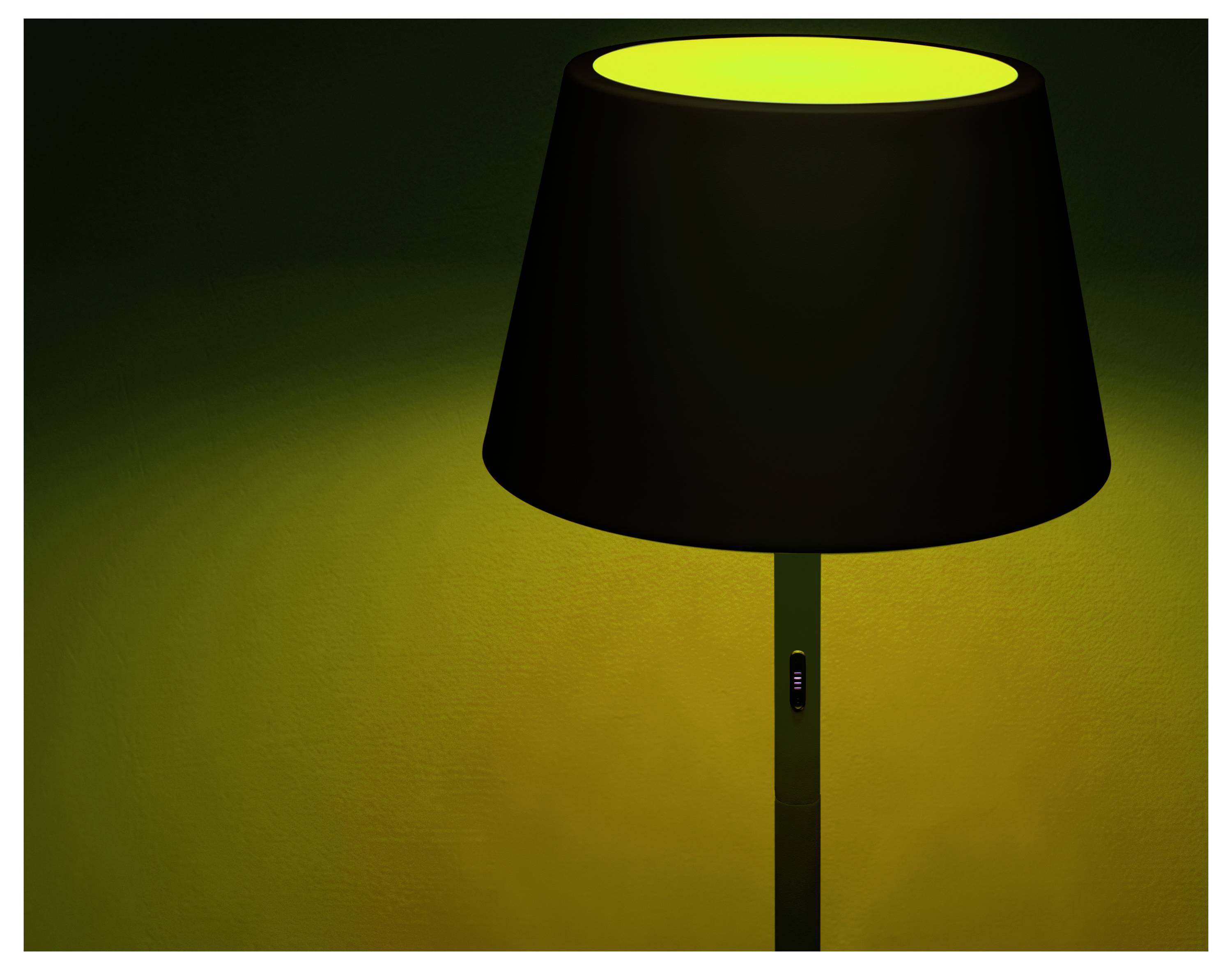 Een zwarte lampenkap met een gloeiend geel licht van binnen, dat een warm geel licht werpt op een donkergroene achtergrond.