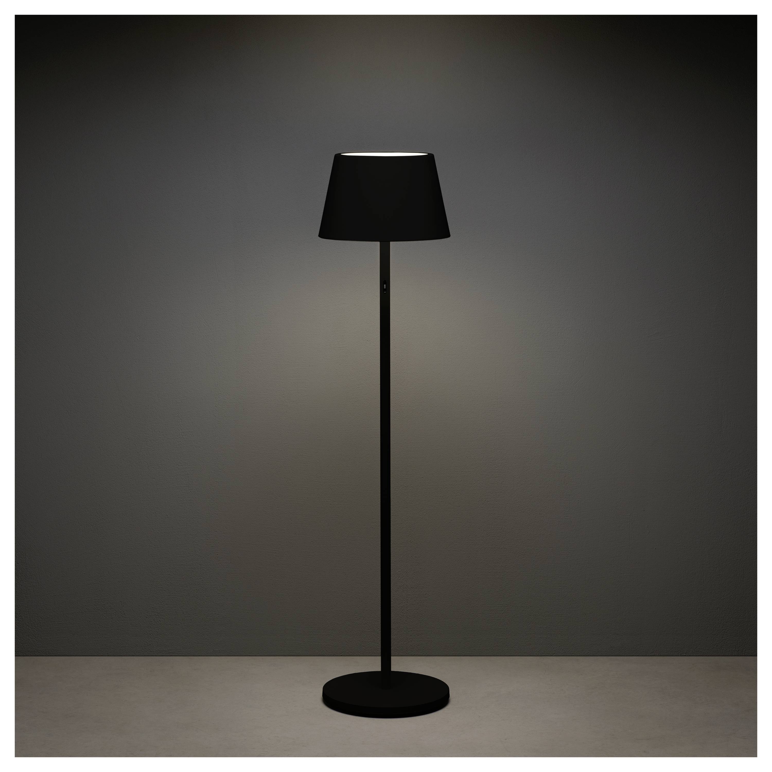 Een slanke, moderne zwarte vloerlamp verspreidt een zacht licht en verlicht de ruimte eromheen tegen een donkergrijze achtergrond.