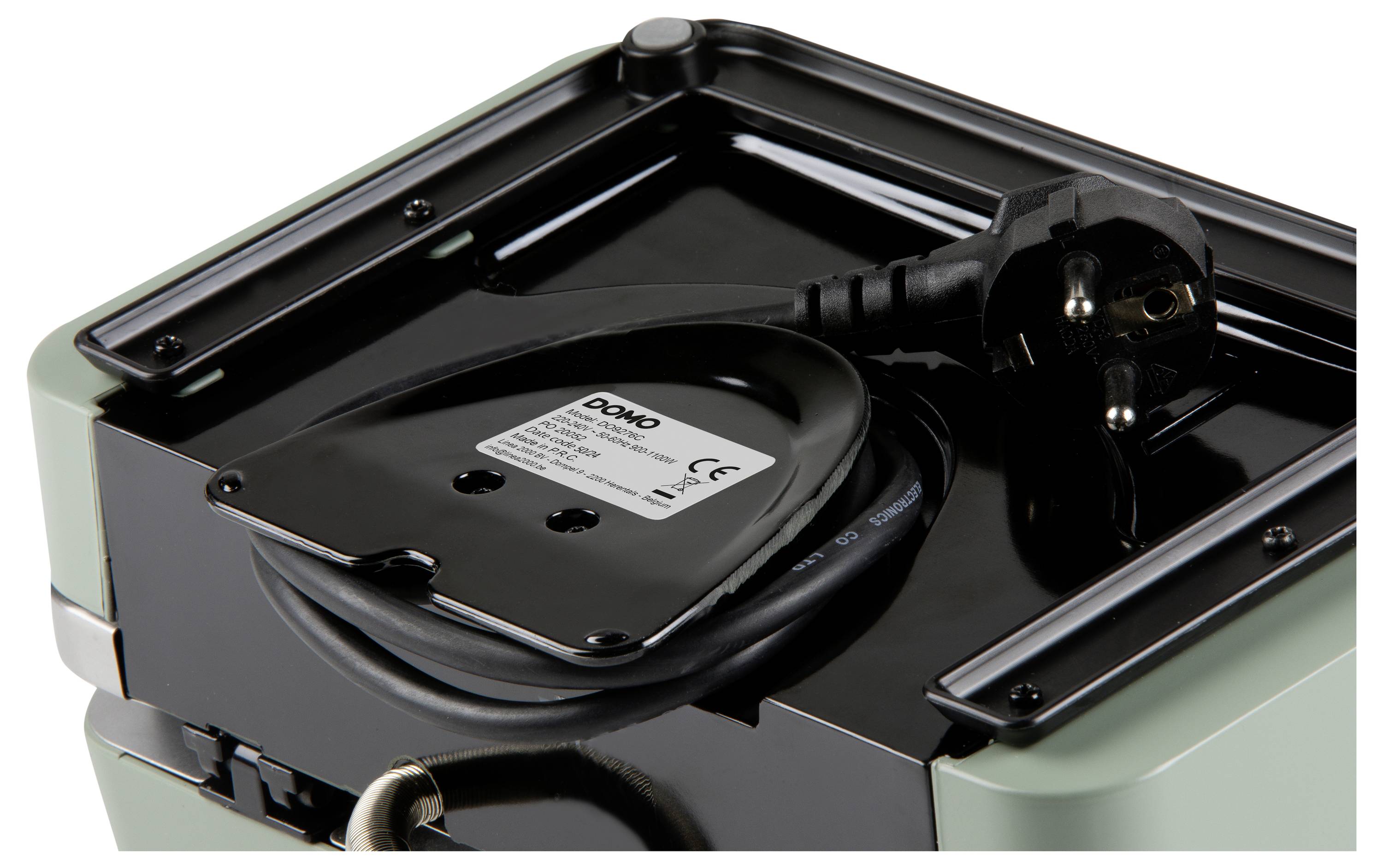 Een close-up van een elektrische stekker en snoer netjes opgeborgen in een compartiment op een apparaat, waarbij een label met veiligheids- en modelinformatie zichtbaar is.