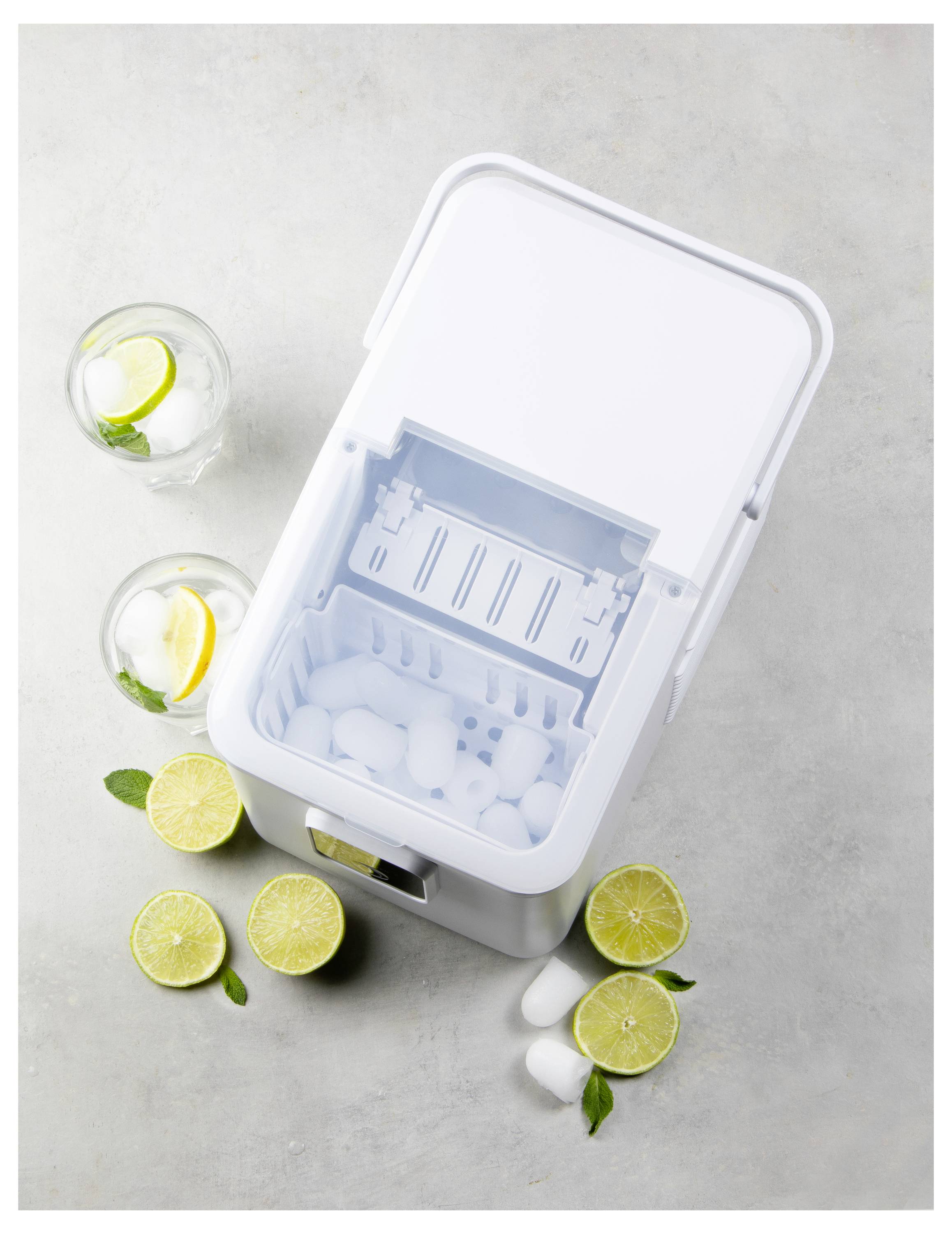 Een witte ijsmachine gevuld met ijsblokjes wordt van bovenaf getoond. Twee glazen met ijs, citroenschijfjes en munt staan naast doorgeknipte citroenen.