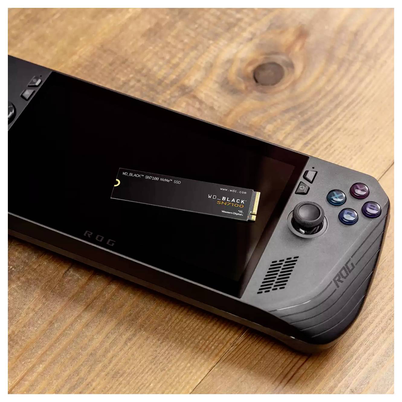 Een draagbare gameconsole rust op een houten oppervlak, met een zwart scherm en gekleurde knoppen aan de rechterkant en een gamekaart die erin is gestoken.