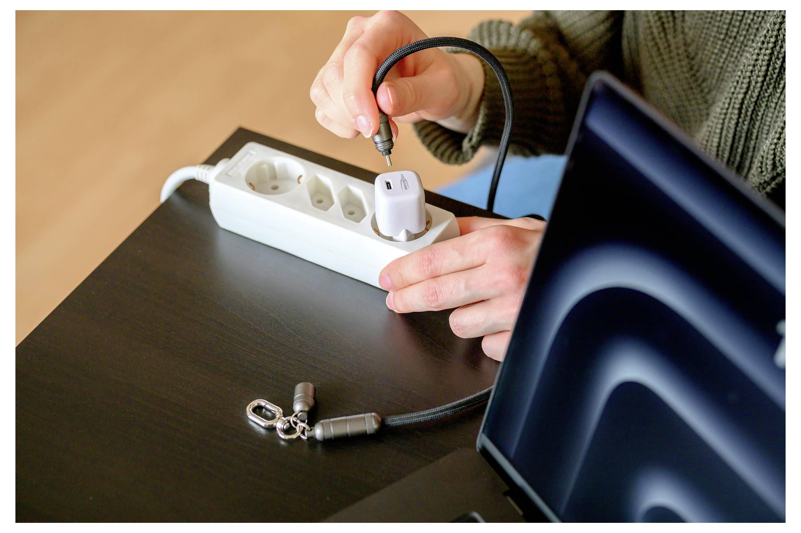 Persoon die een beveiligingskabel met slot bevestigt aan een laptop op een bureau met een stekkerdoos in de nabijheid.
