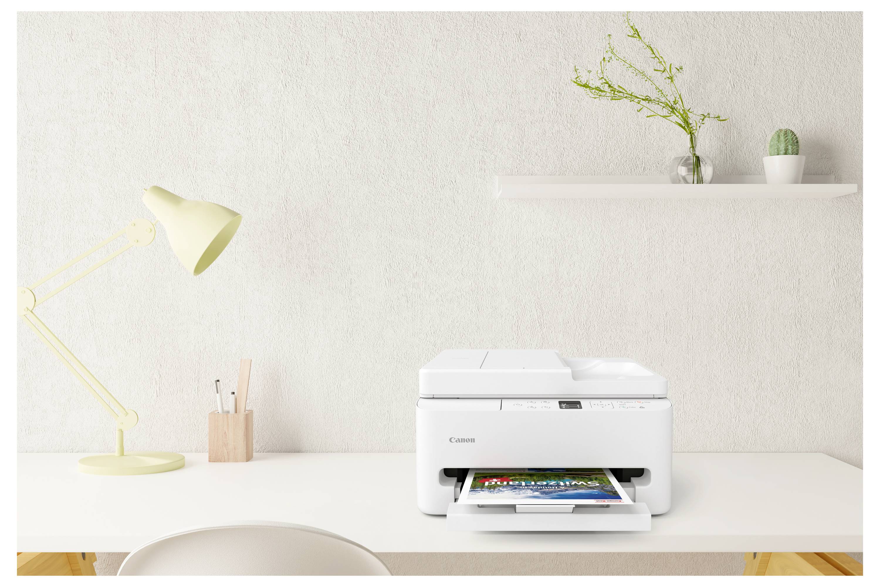 Een witte printer op een bureau drukt een kleurrijke foto af. Een lamp en kantoorartikelen bevinden zich links, met een plank en planten op de achtergrond.