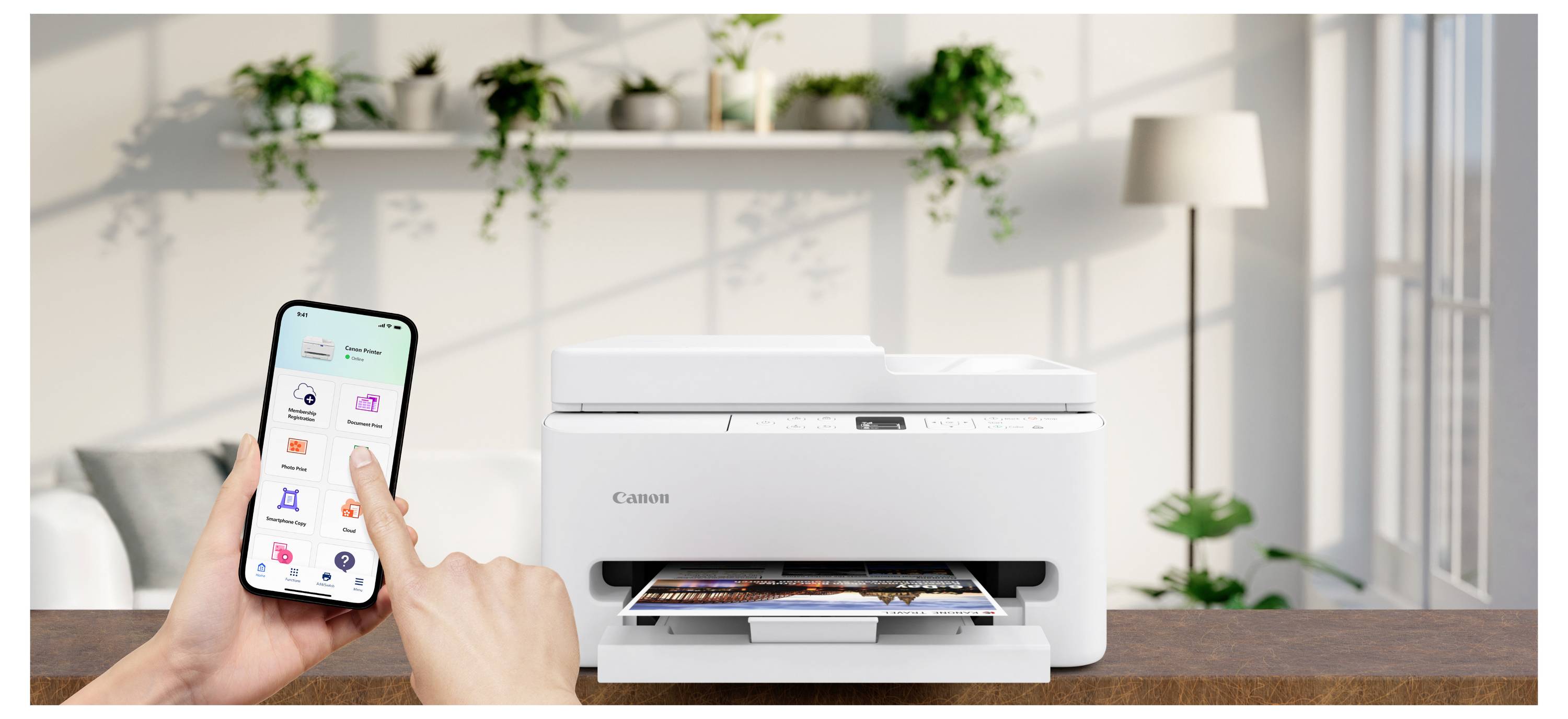 Een persoon bedient een witte printer op een houten oppervlak met een smartphone in een lichte ruimte met planten op de achtergrond.