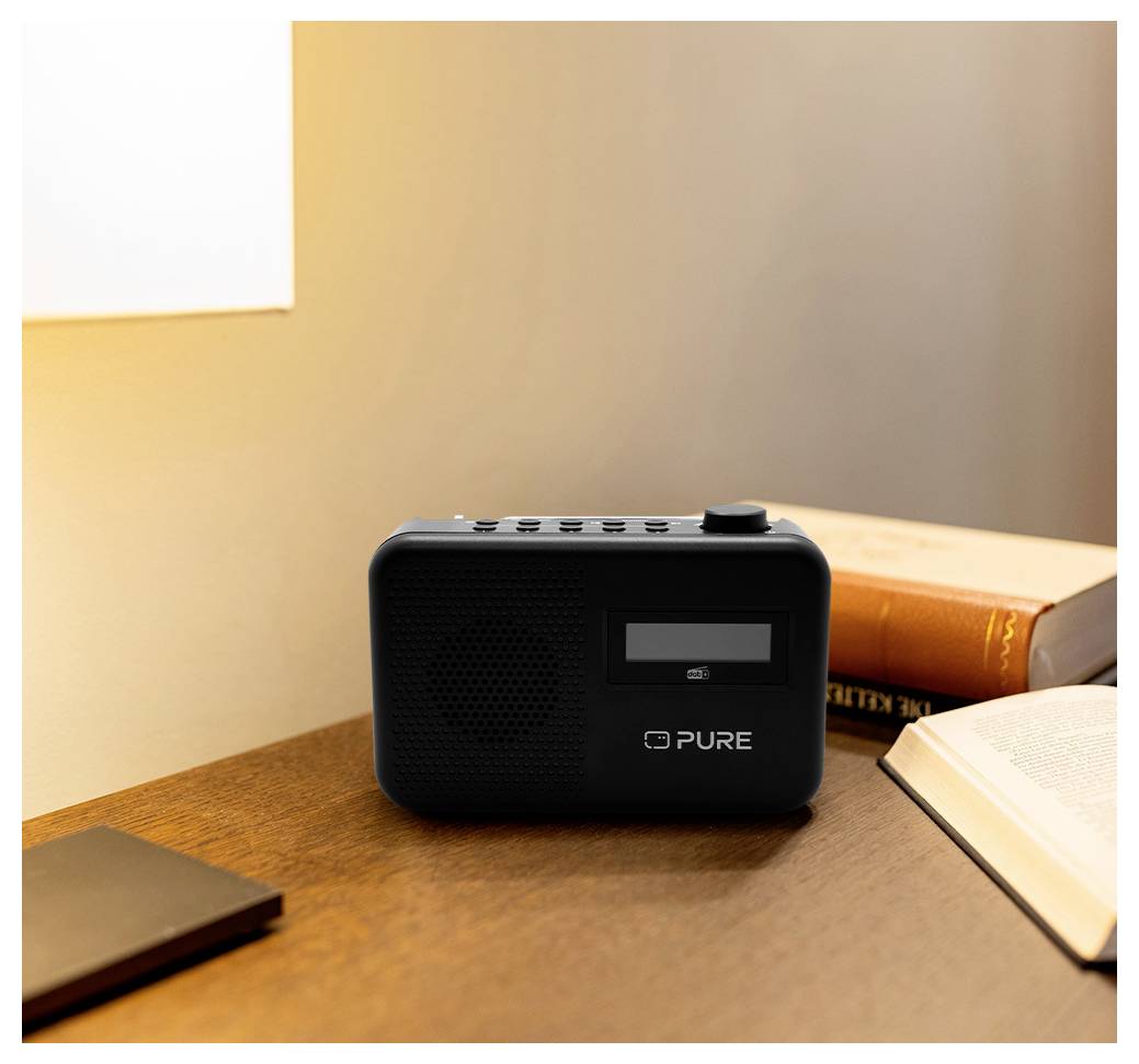 Een digitale radio op een houten bureau naast een gesloten boek, dat zacht licht uitstraalt in een warmverlichte ruimte.