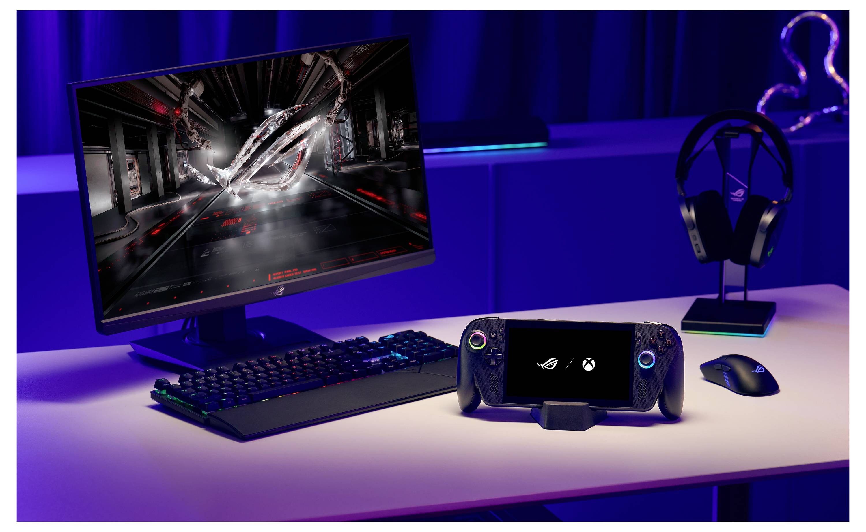 Een desktopopstelling met een gamingmonitor, toetsenbord, draadloze koptelefoon en een draagbare gamingapparaat op een tafel, allemaal in een donker verlichte ruimte.