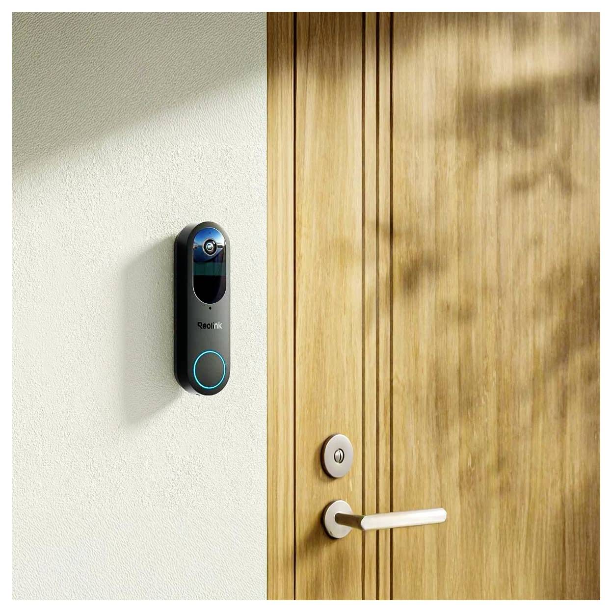 Een slimme deurbel geïnstalleerd op een muur naast een houten deur, voorzien van een camera en knop.