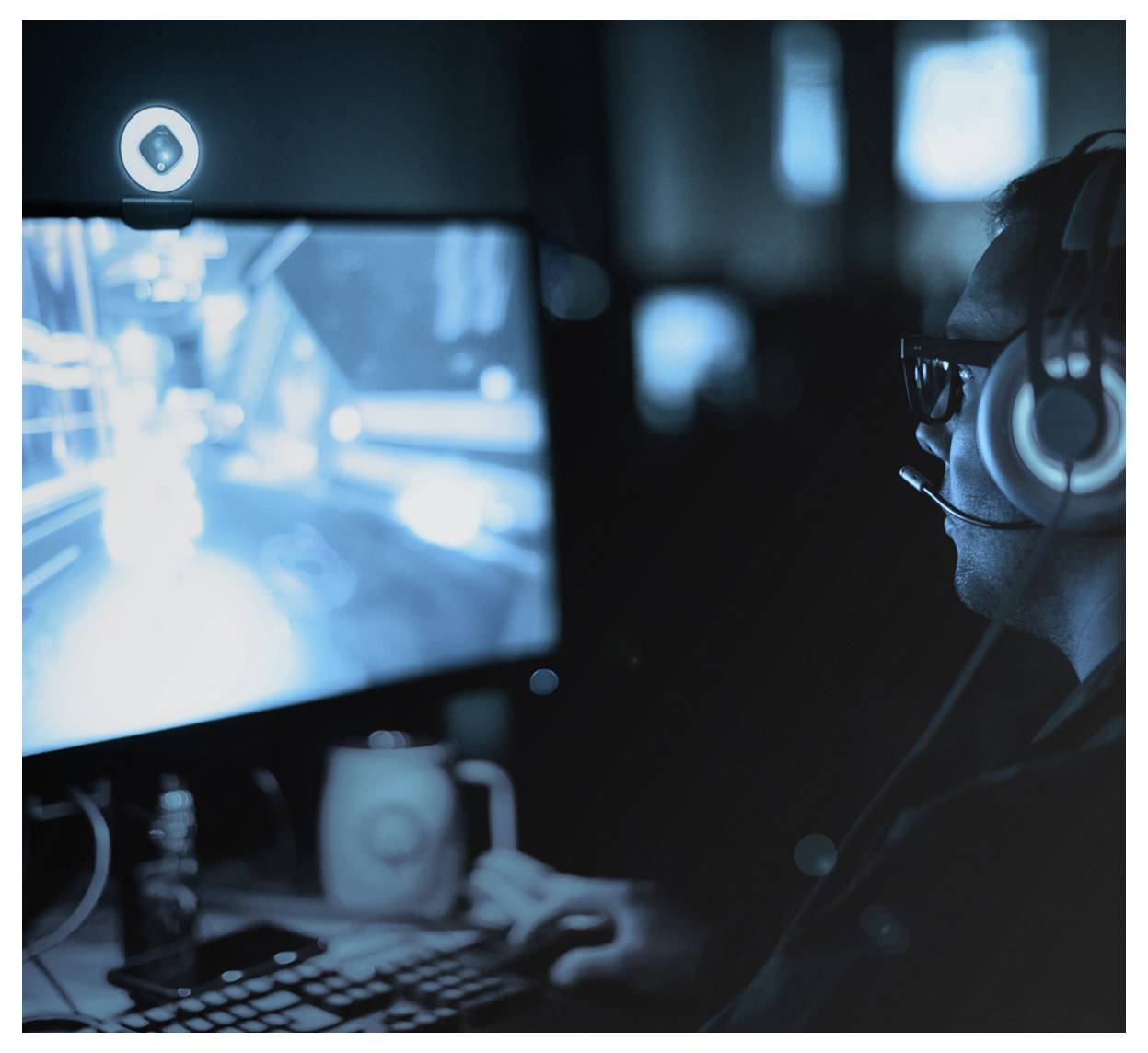 Een persoon met een headset is aan het gamen op een computer in een donker verlichte ruimte, gefocust op het scherm met een drankje naast zich.