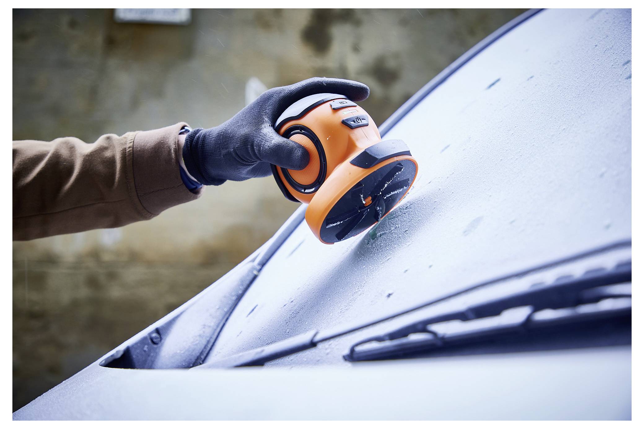 Een persoon met een handschoen gebruikt een oranje en zwart gereedschap om condensatie van een autoruit te verwijderen.