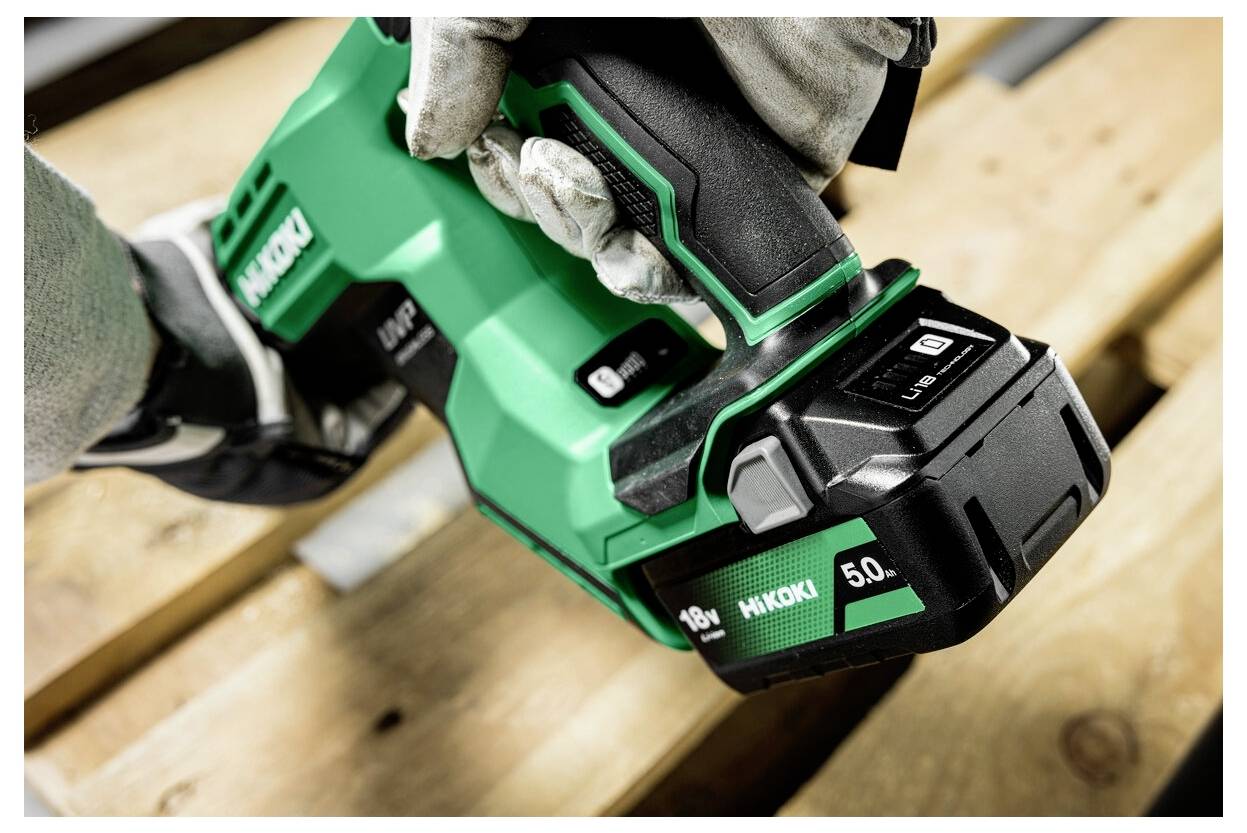 Een persoon met handschoenen houdt een groene Hikoki-powergereedschap vast, waarbij hij deze naar beneden drukt op een houten pallet oppervlak.