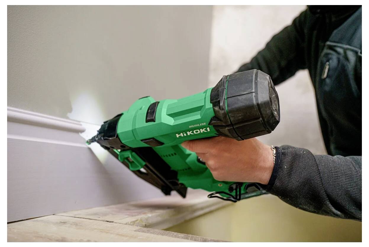 Een persoon die een groene spijkerpistool gebruikt om plinten aan de muur te bevestigen, waarbij een klus voor woningverbetering wordt gedemonstreerd.