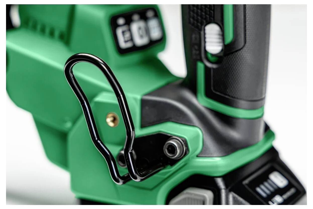 Close-up van een groene en zwarte handgreep van een gereedschap met een metalen clip bevestigd, waarbij een deel van een digitaal scherm zichtbaar is.