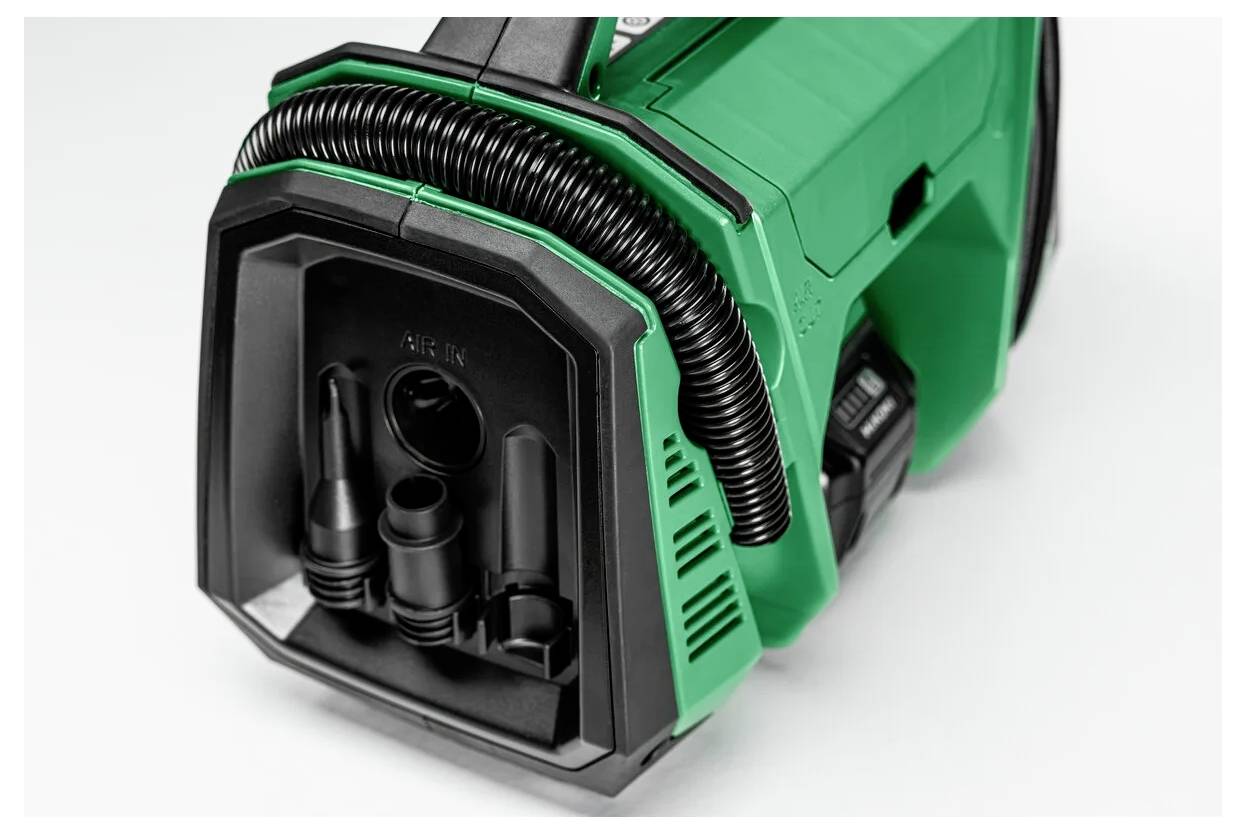Een groene en zwarte draagbare werkplaatsstofzuiger met een gewonden slang, meerdere mondstukken en een stevig handvat, geschikt voor het reinigen van gereedschap en oppervlakken.