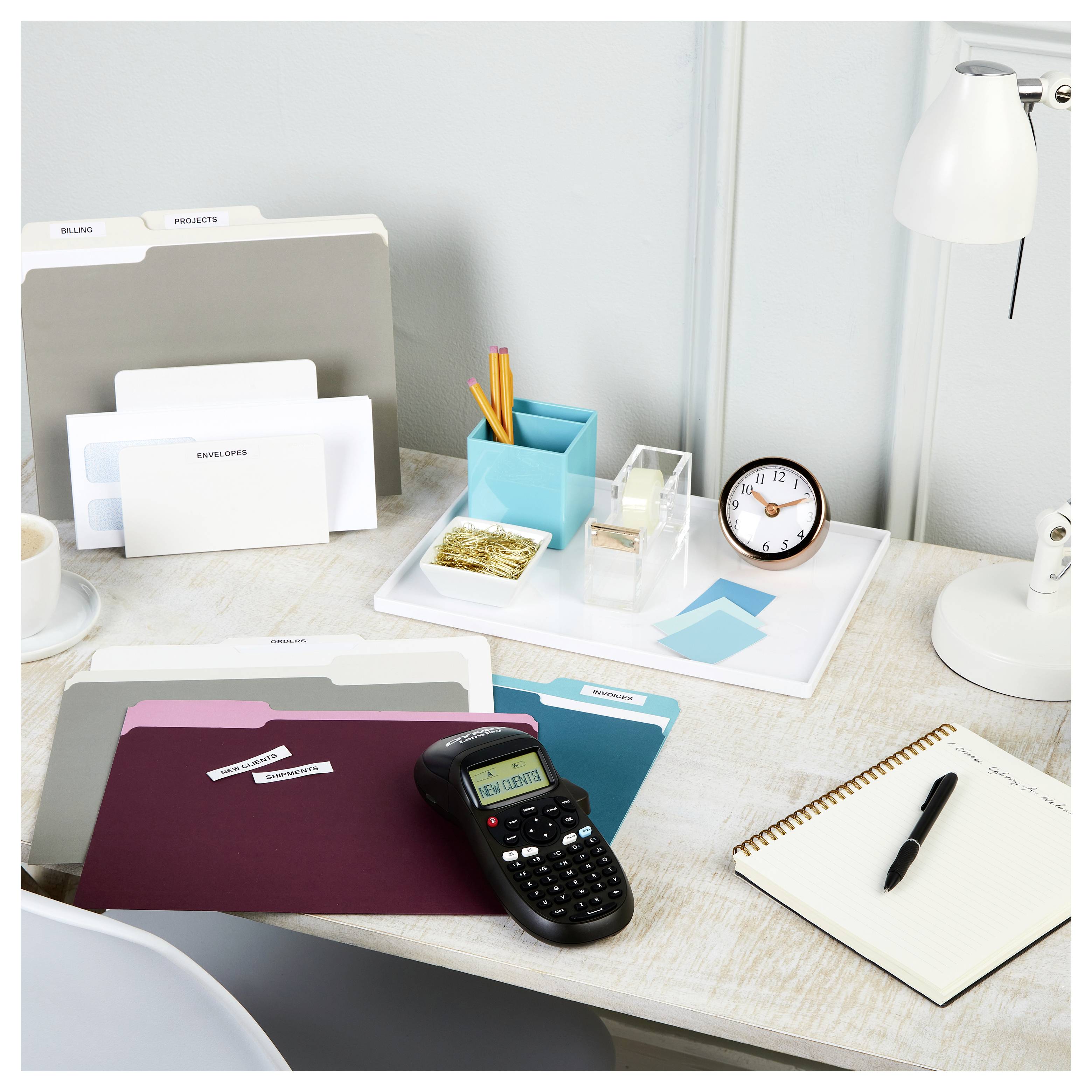 Een netjes georganiseerd bureau met mappen, een labelmaker, pennen in een houder, een notitieboek en een klok, wat een efficiënte werkplek uitstraalt.