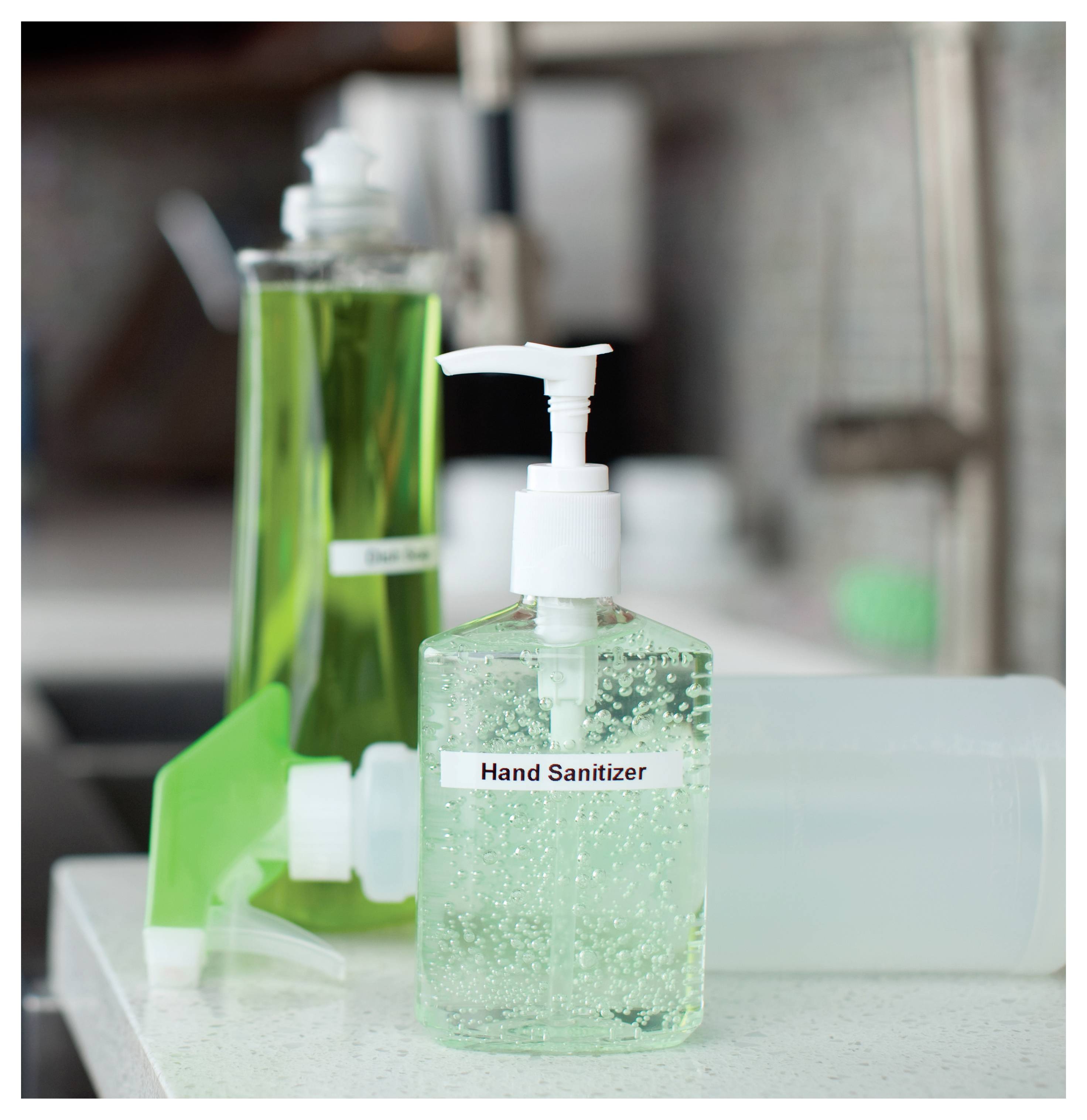 Een flesje handdesinfectans met een pomp op een aanrecht, gelabeld 'Handdesinfectans', naast andere schoonmaakproducten en een gootsteen.