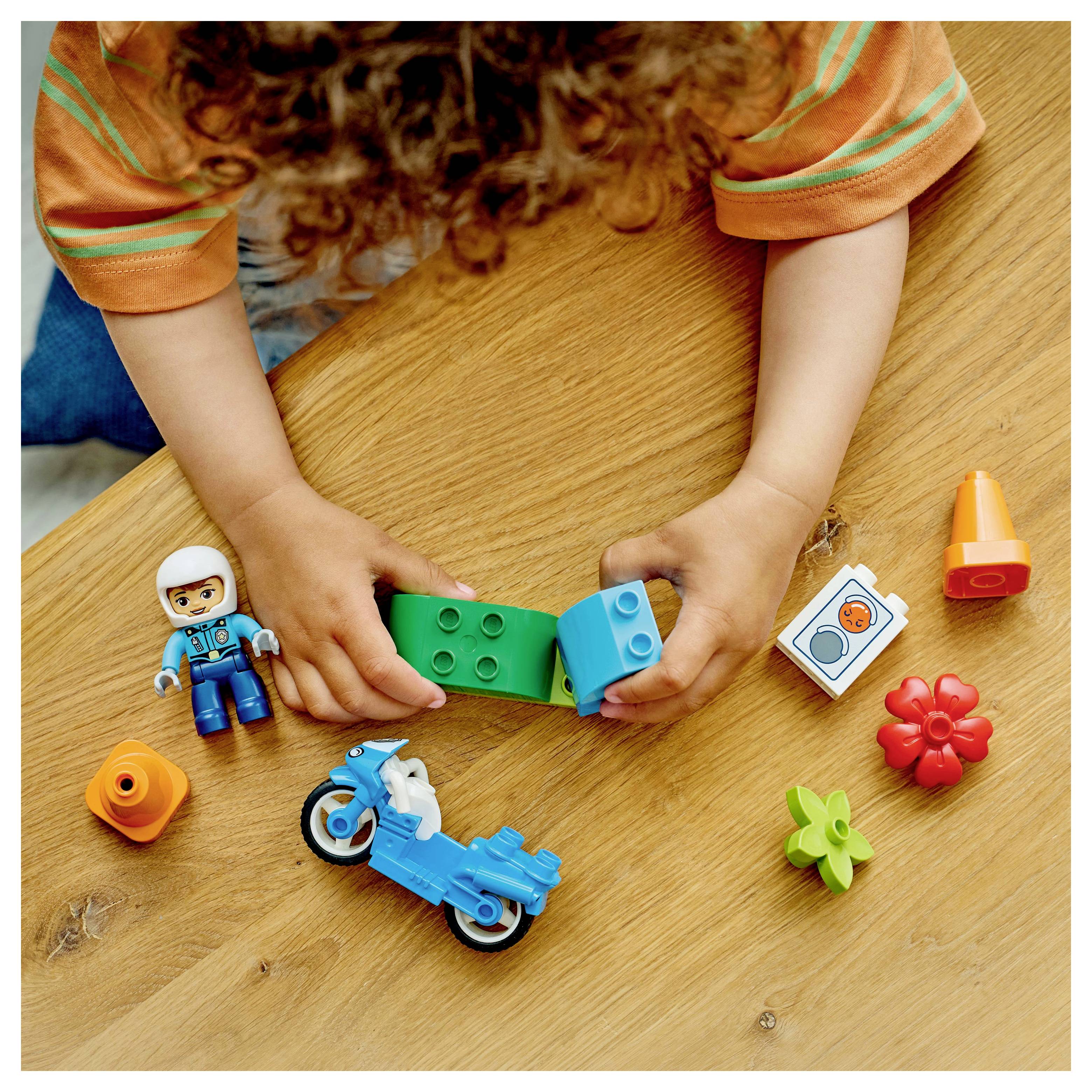 Een kind dat met kleurrijke speelgoedblokken op een tafel bouwt, inclusief een miniatuurfiguur, motorfiets en verschillende vormen.
