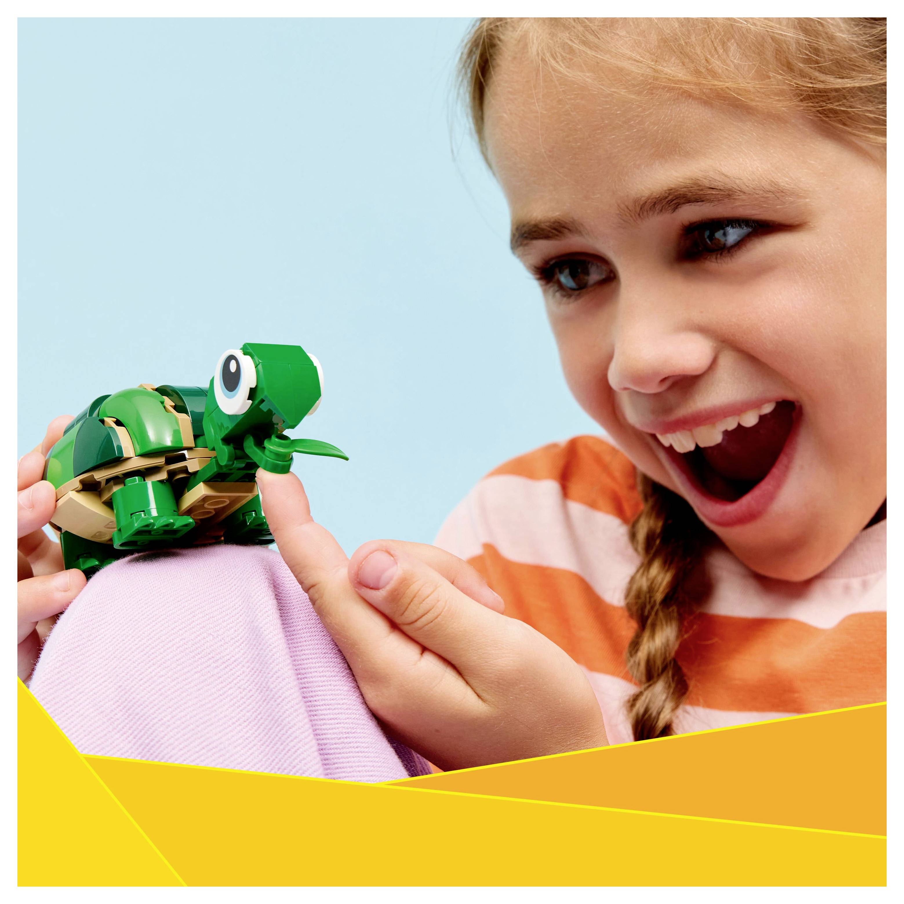 Een kind interageert enthousiast met een kleine, groene schildpadpop, waarbij vreugde en speelsheid worden tentoongespreid tegen een pastelblauwe achtergrond.