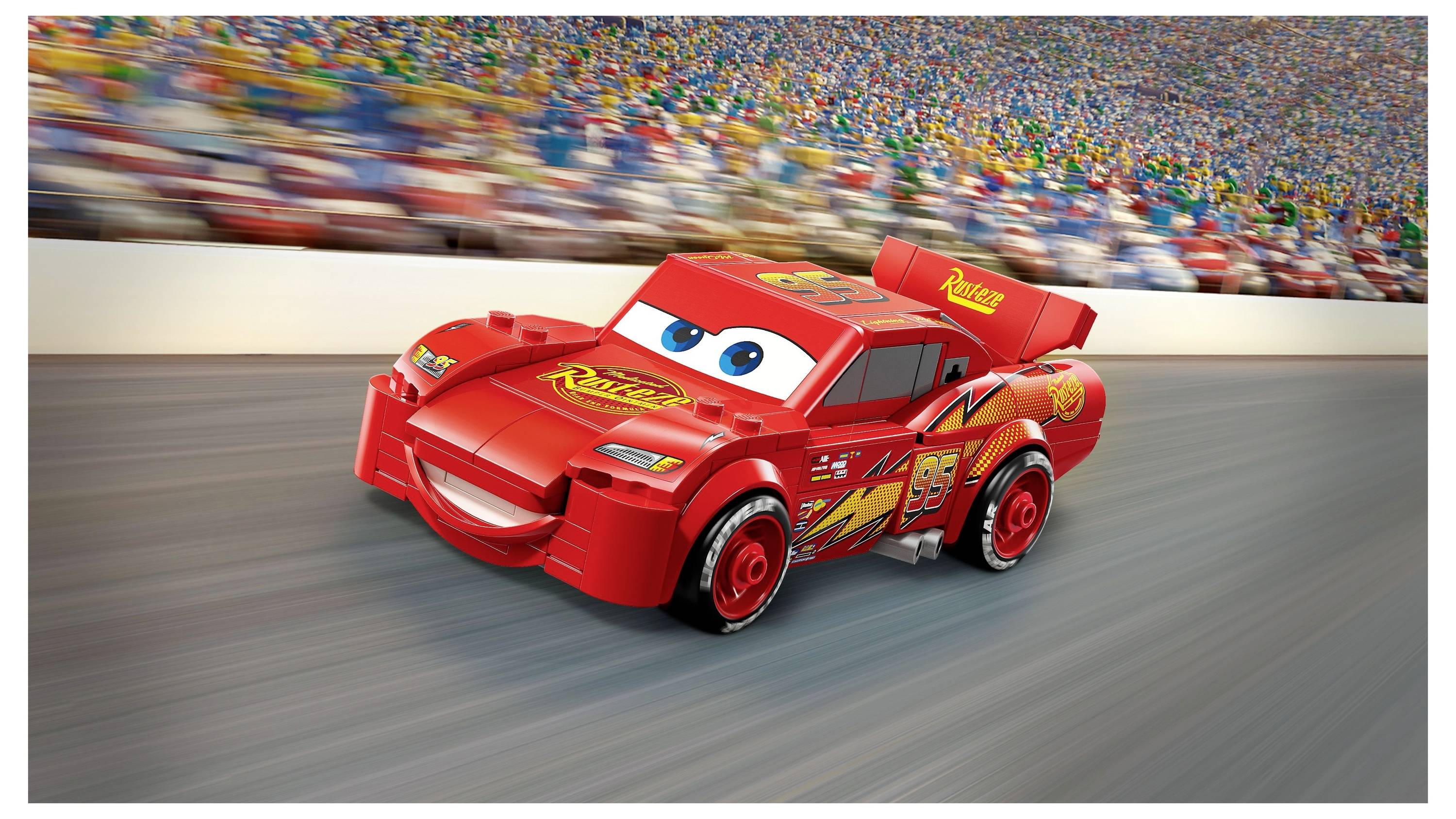 Een speelgoed raceauto met ogen en een mond, die lijkt op een personage uit een film, raast over een racecircuit met een wazig publiek op de achtergrond.