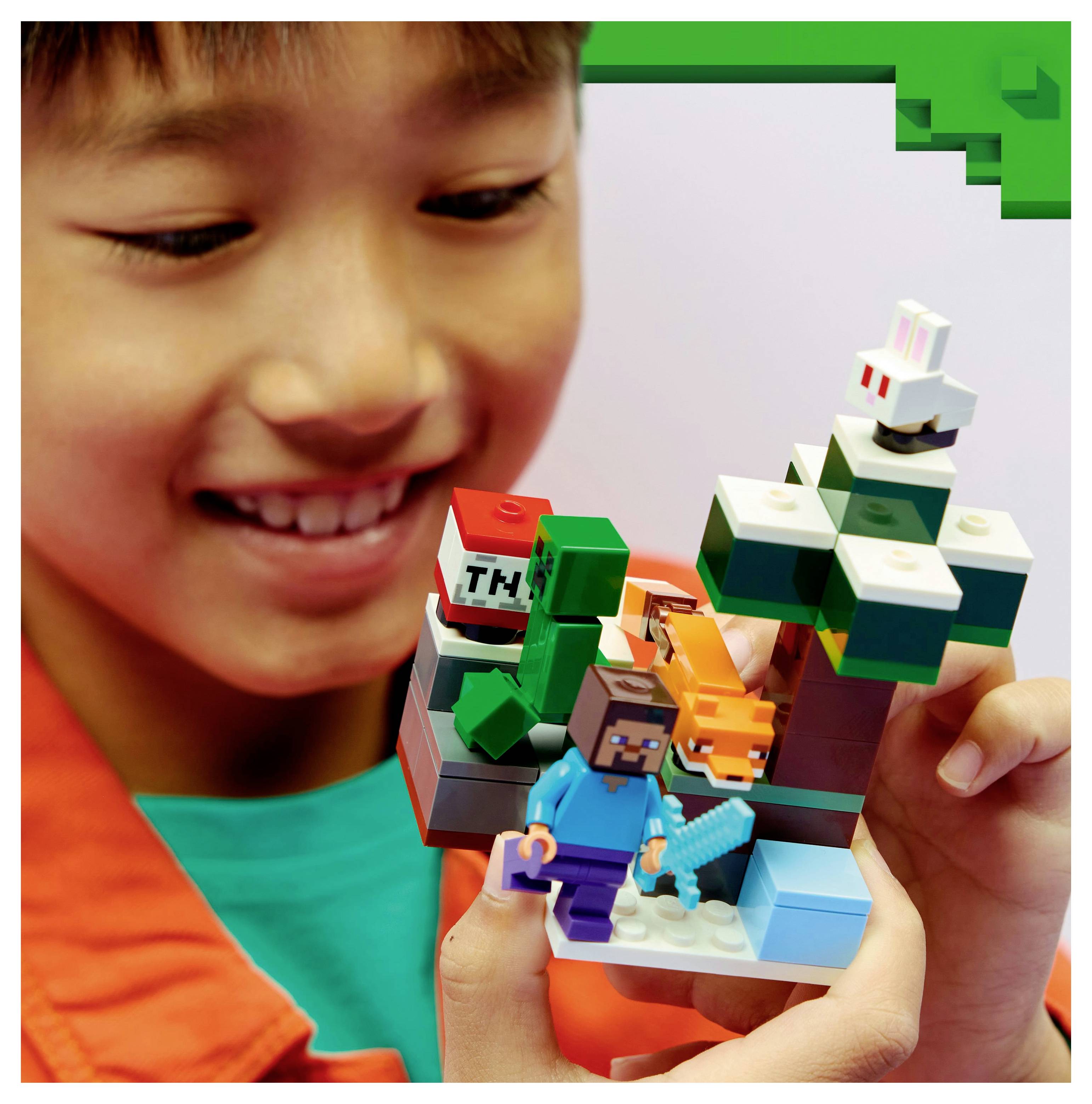 Een kind dat een LEGO Minecraft-set vasthoudt met iconische personages en elementen zoals een boom, vos, Creeper en TNT-blok, lacht met opwinding.