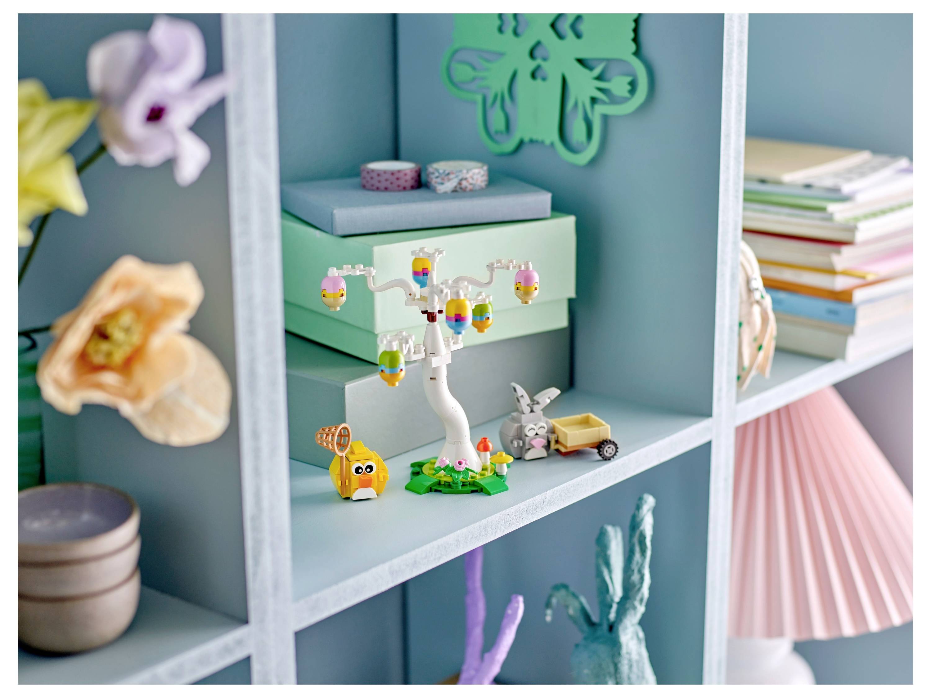 Een kleurrijke plankdisplay met pastelkleurige dozen, bloemen, decoratieve speelgoed en een kleine lamp, die een speelse en artistieke sfeer creëert.