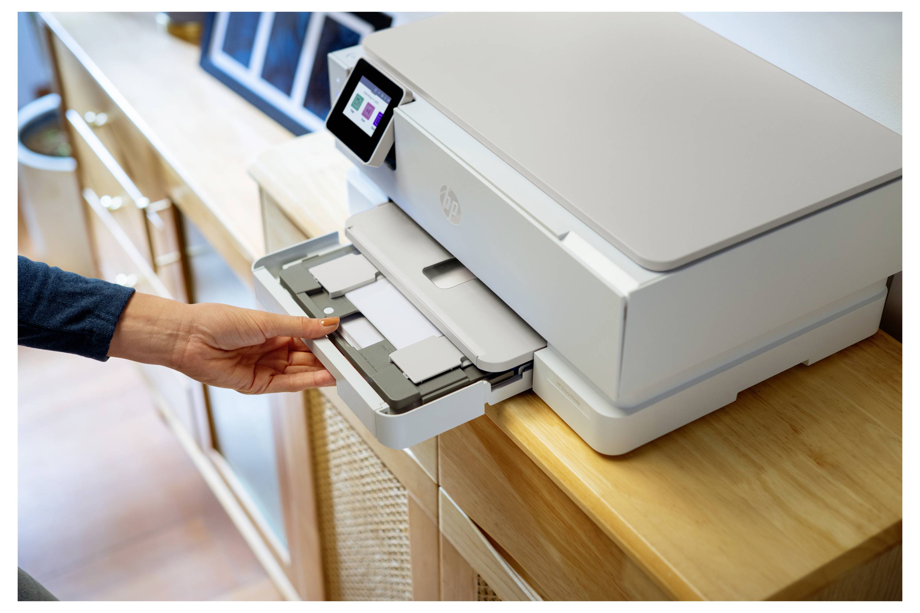 Een persoon plaatst een document in de papierlade van een witte printer in een goed verlichte ruimte. De printer heeft een klein digitaal display.