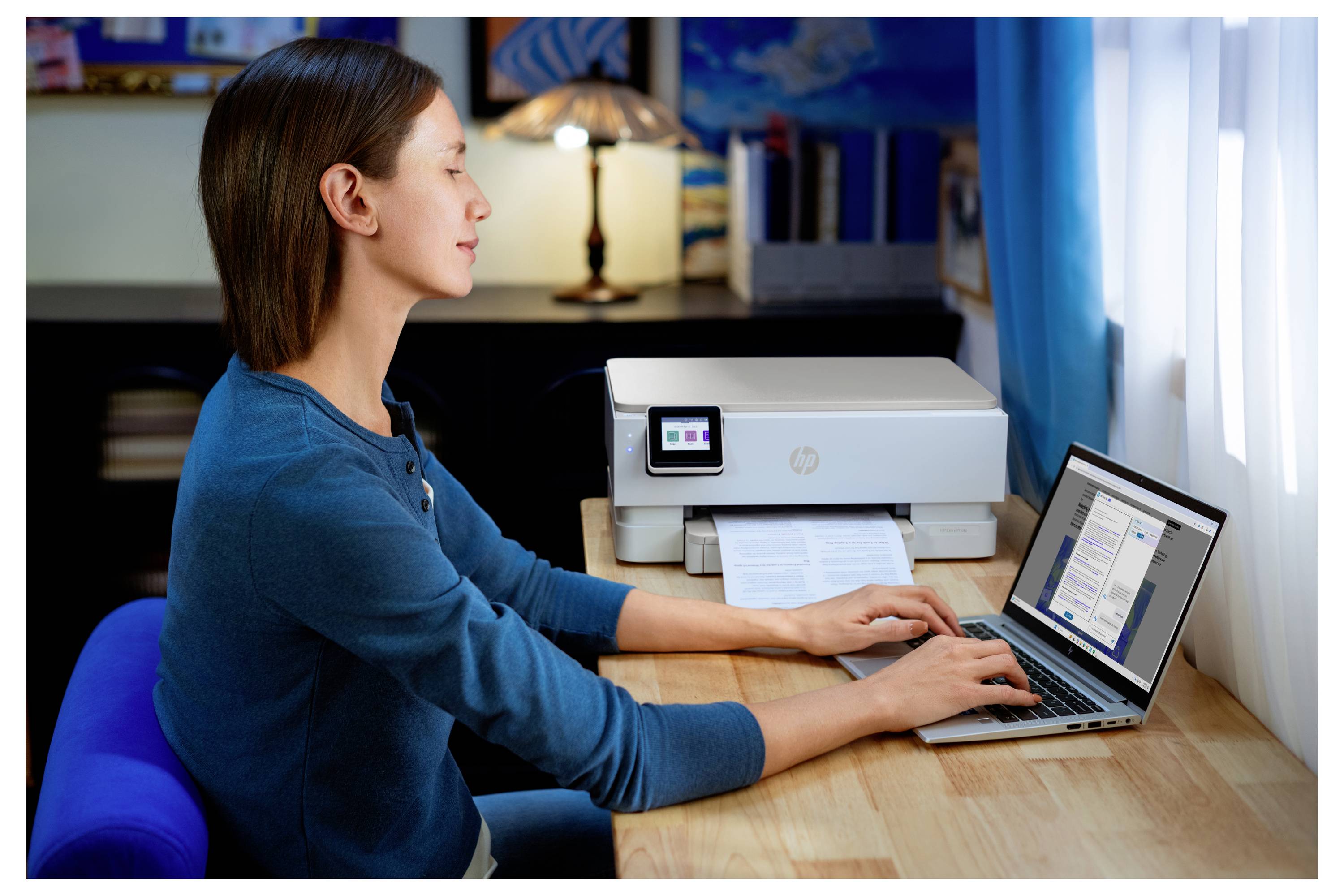 Een persoon die een laptop gebruikt naast een printer op een bureau in een thuiskantoor, wat suggereert dat een afdruktaak bezig is.