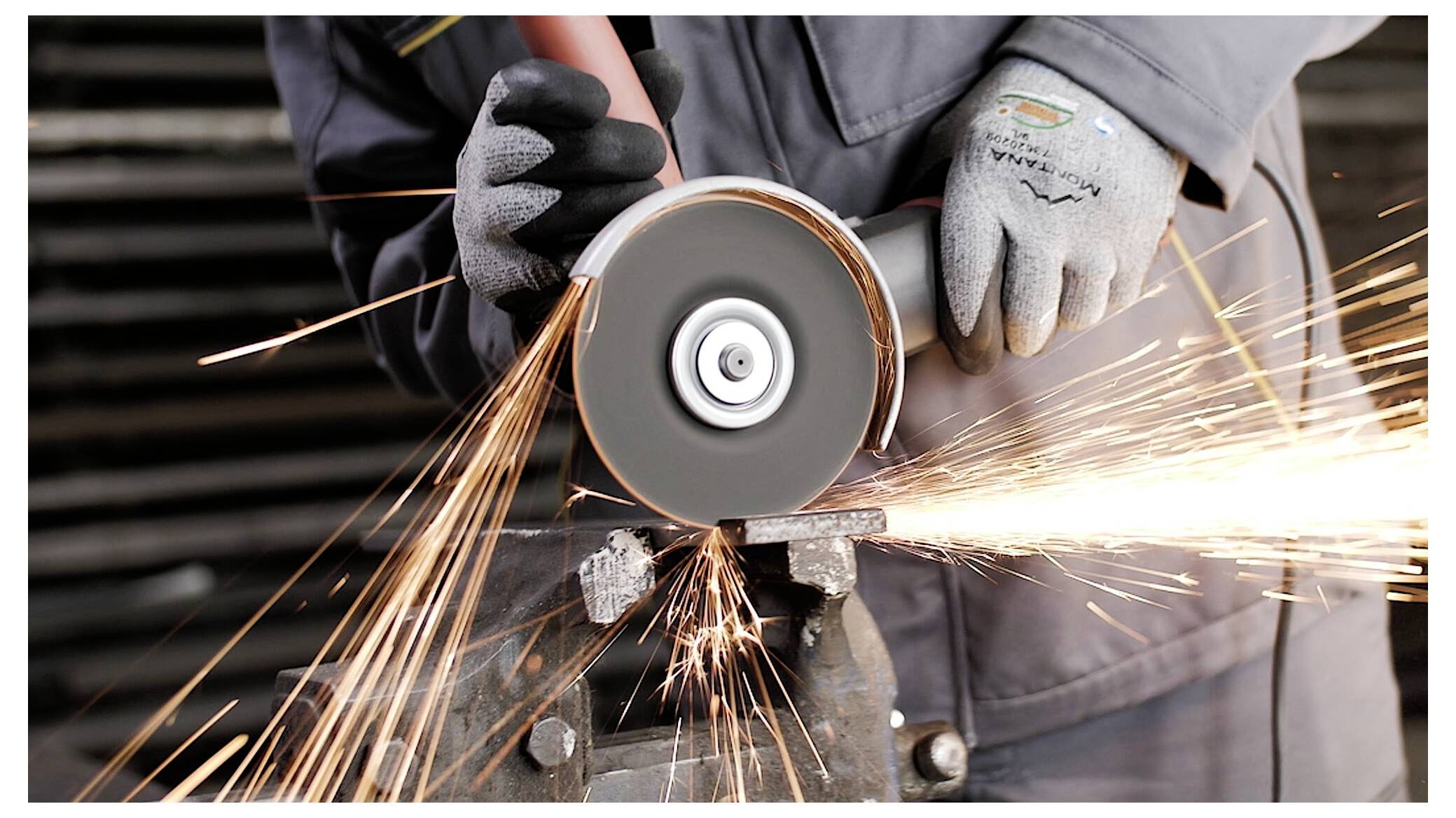 Een persoon met handschoenen gebruikt een haakse slijpmachine, waarbij felle vonken vrijkomen. De focus ligt op het gereedschap en de beweging van het doorsnijden van metaal.