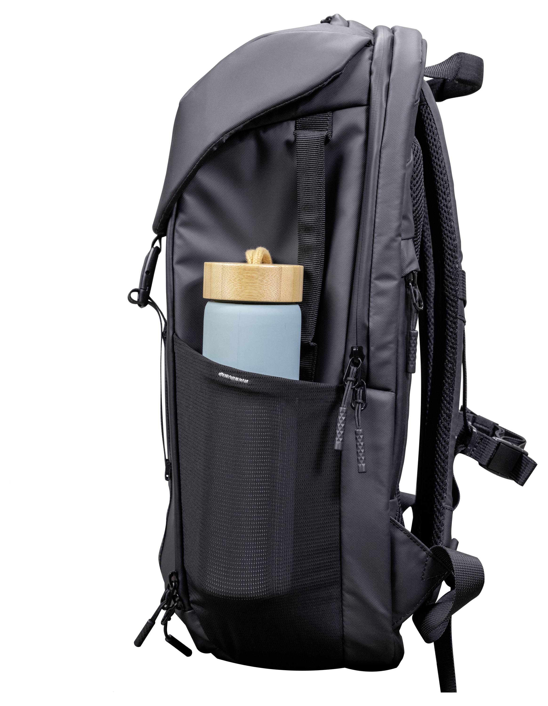 Een zwarte rugzak met een zijdelings gaasnetje dat een blauwe waterfles met een houten deksel vasthoudt. De rugzak heeft gewatteerde draagriem en meerdere ritsen.