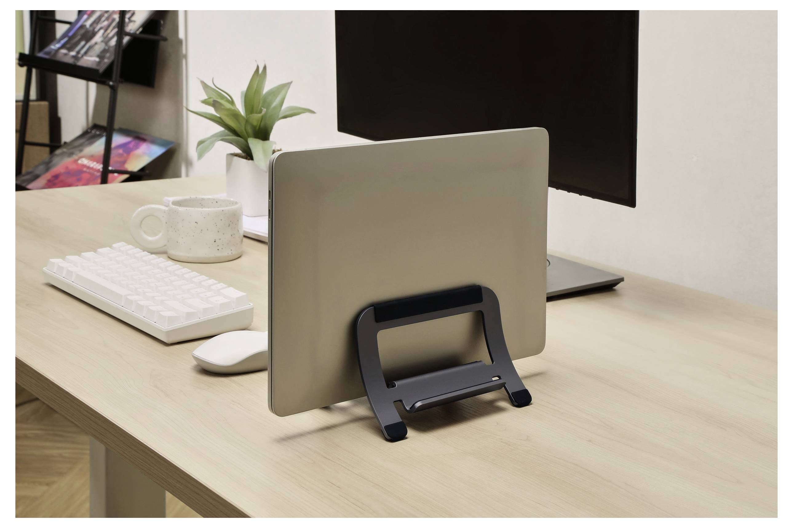 Een laptop in een standaard op een houten bureau met een toetsenbord, mok en plant, geplaatst in een kantooromgeving.