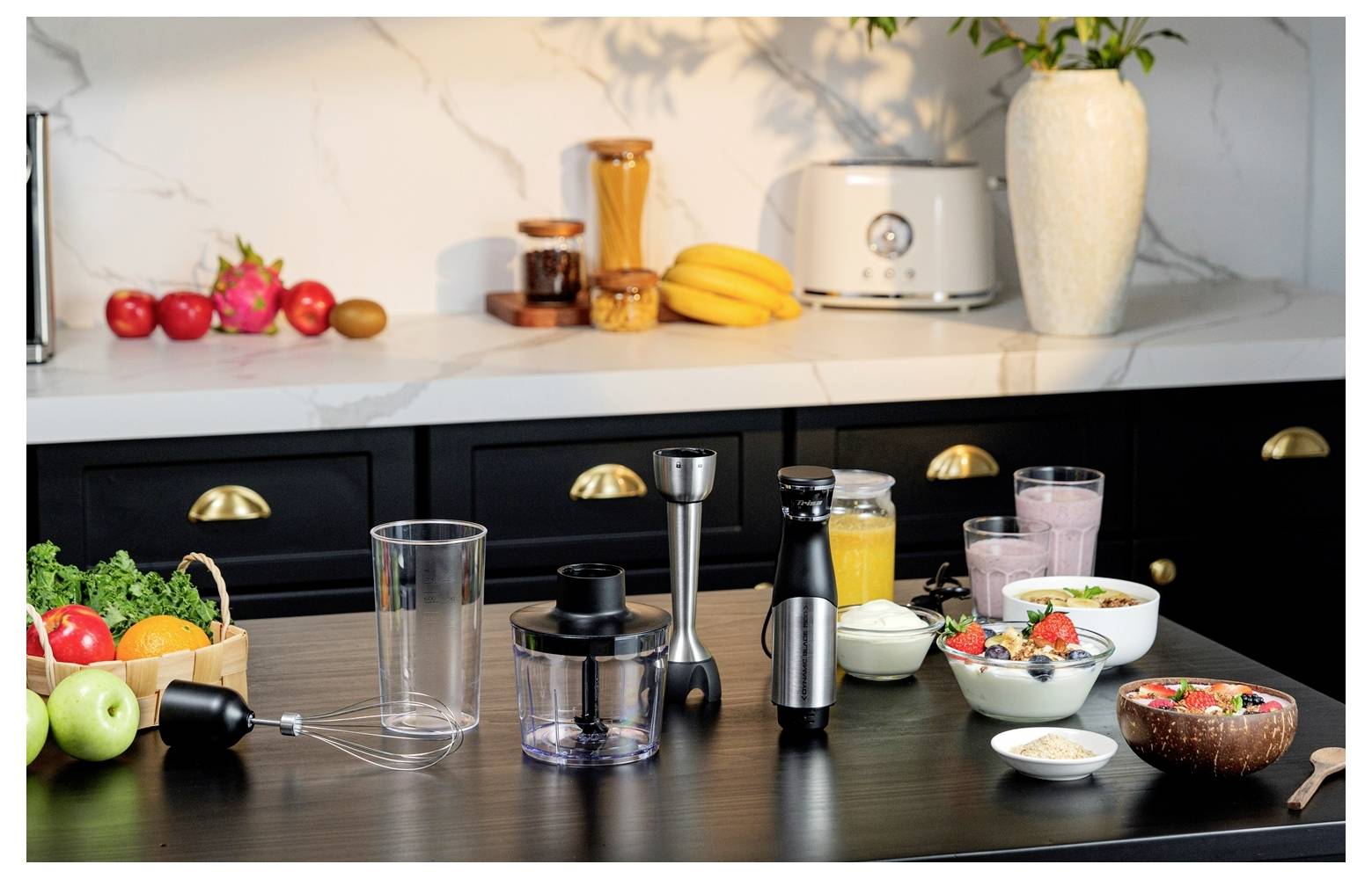Een aanrecht in de keuken met een blender, verse vruchten, smoothies en yoghurtbowls. Keukenapparatuur en decoratie zijn op de achtergrond zichtbaar.