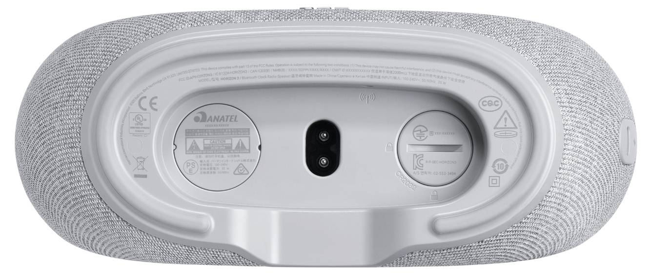 De afbeelding toont de achterkant van een grijze ovale speaker met een voedingsingang, USB-poort en fabrikantinformatie met regelgevingspictogrammen.
