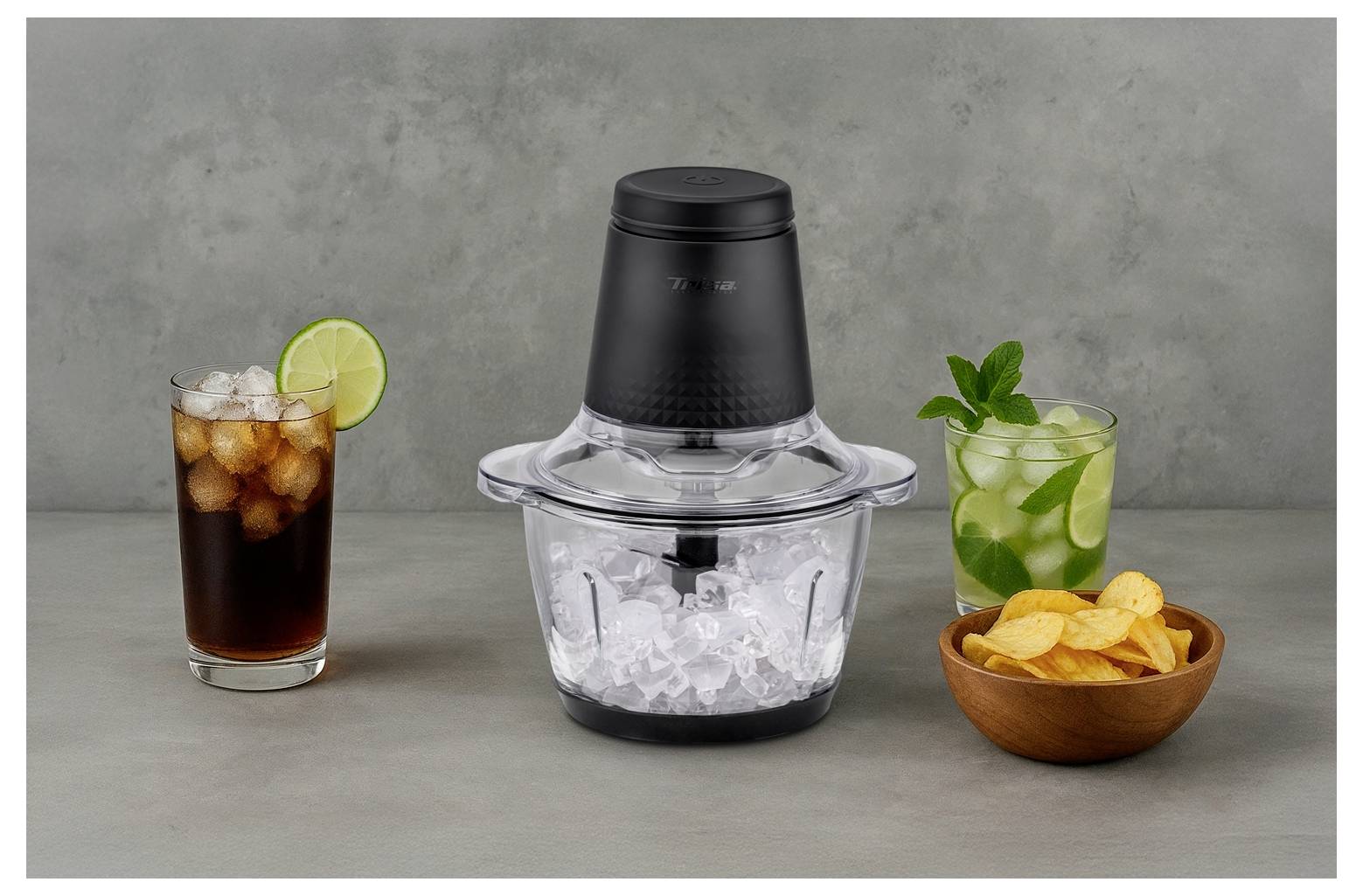 Een zwarte en transparante ijscrusher staat centraal, omringd door een cola met limoen, een mojito met munt, en een kom met aardappelchips.