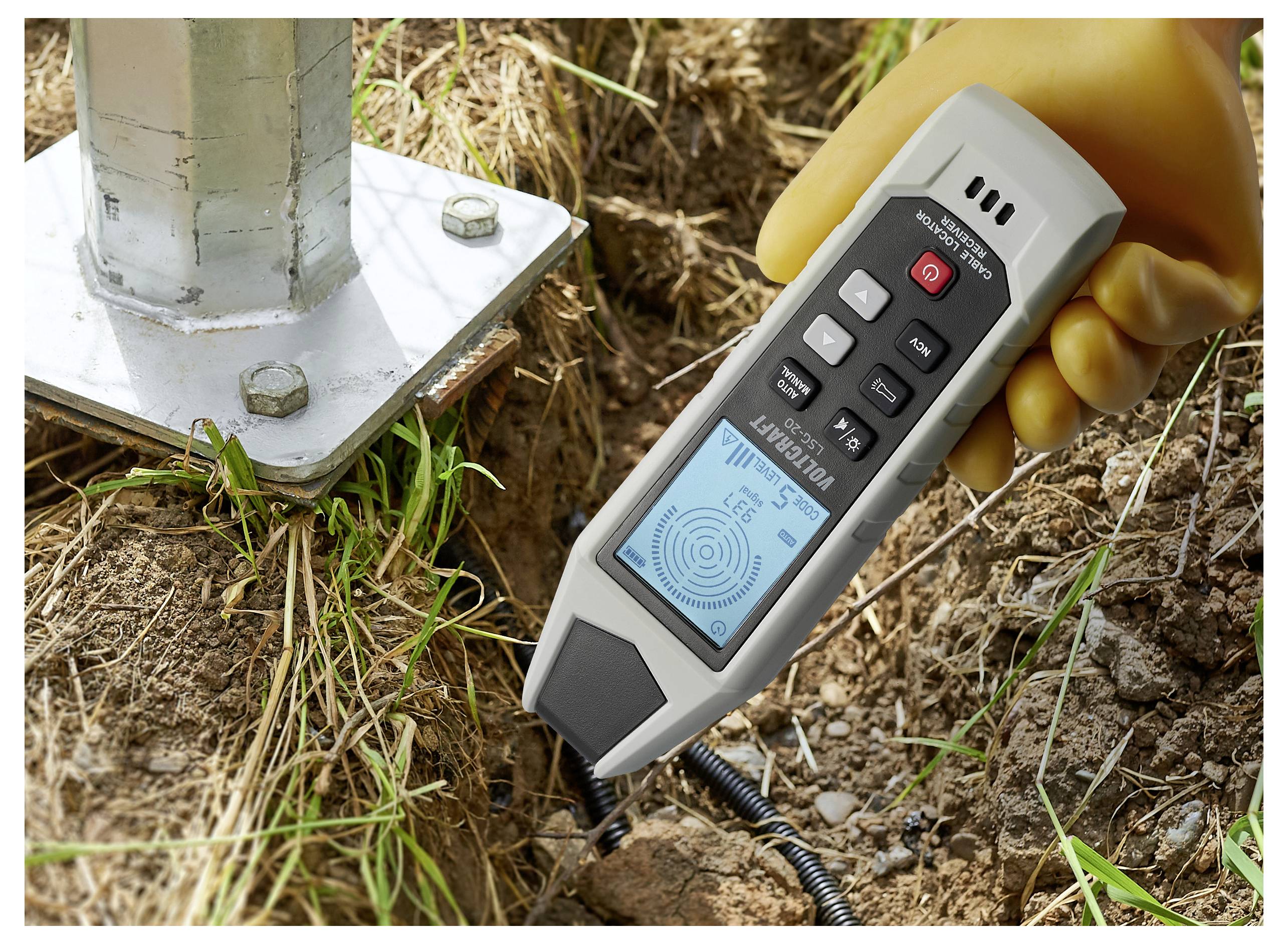 Een persoon gebruikt een handheld elektromagnetische veldsterktemeter in de buurt van een metalen paalvoet buiten, controleren signaallezingen op het display.