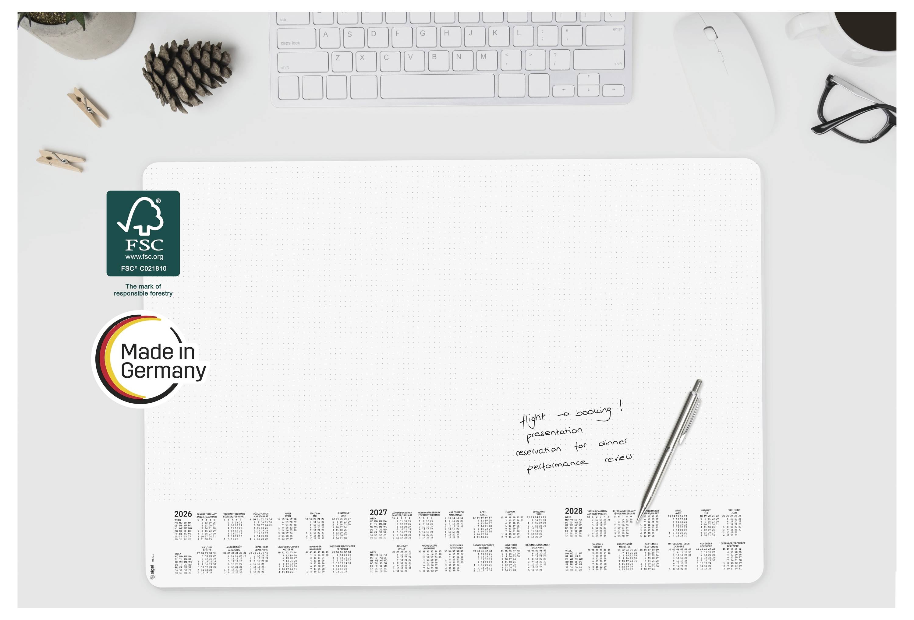 Minimalistische bureauplanner of scheurkalender op een wit bureau, voorzien van FSC- en 'Made in Germany'-logos, met toetsenbord en pen in de buurt.
