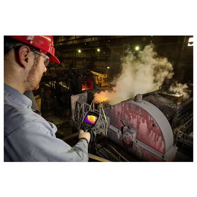 Een werknemer met een rode helm en veiligheidsbril gebruikt een thermische beeldvormingsapparatuur om industriële apparatuur die stoom uitstoot in een fabriek te inspecteren.