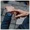 Een persoon met een donkere mouw controleert een smartwatch die de tijd '8:47' weergeeft op een wazig stenen bestratingsachtergrond.