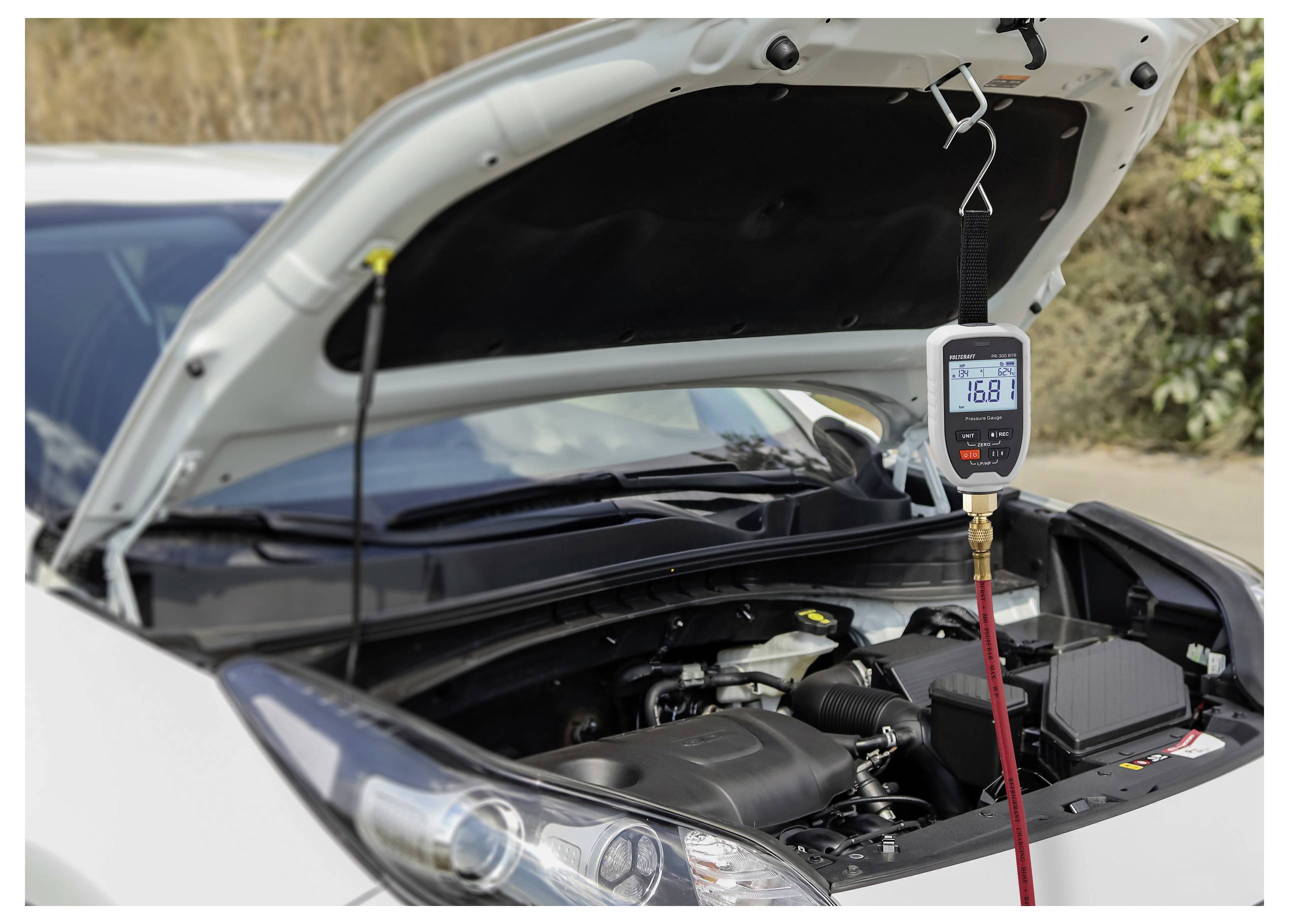 Een auto met open motorkap met een airconditioning manometer die '16.8' psi weergeeft, wat aangeeft dat het druckniveau van het A/C-systeem wordt gecontroleerd.