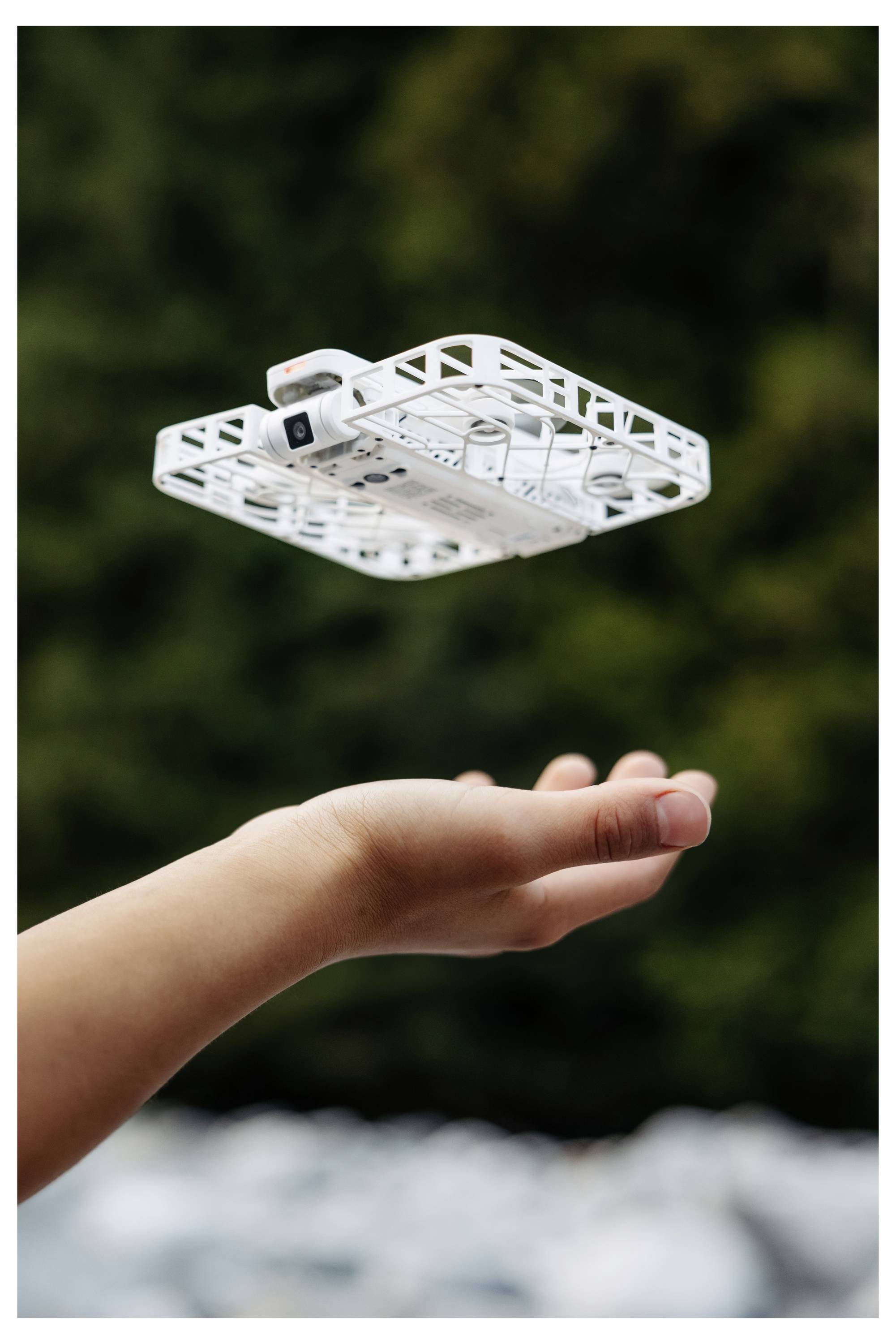 Een kleine drone zweeft boven een uitgestoken hand tegen een wazig natuurlijk decor, wat wijst op vangen of loslaten.