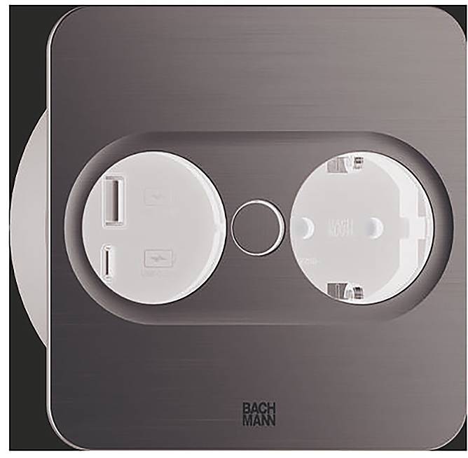 Een close-up van een moderne, metalen dubbele stopcontact met USB-poorten en een ronde knop in het midden, gemerkt met 'Bachmann'.