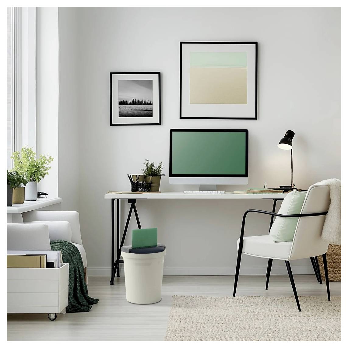 Een modern thuiskantoor met een bureau, computer en groene stoel. Twee kunstwerken hangen aan de muur, met een lamp en plant op het bureau.