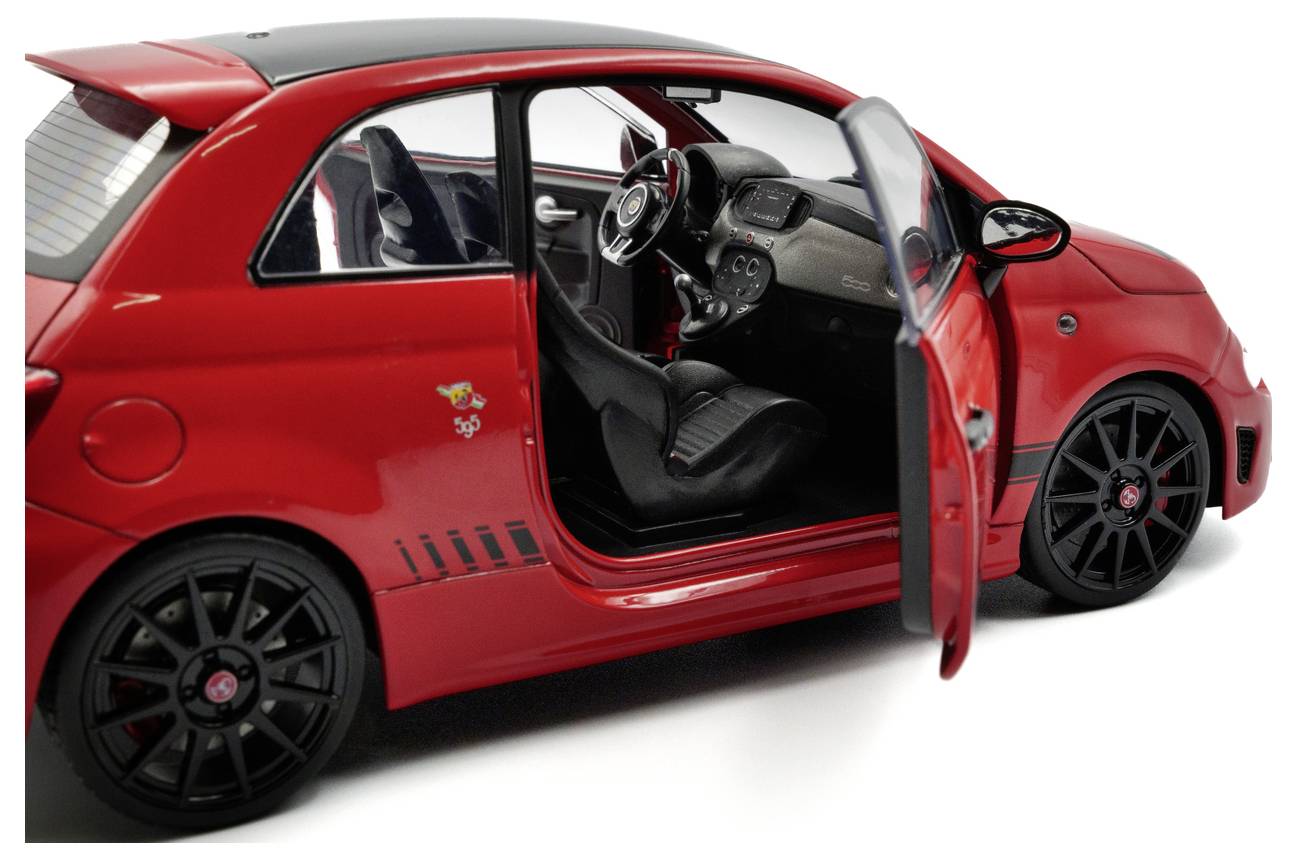 Een rode sportwagen met de voorste passagiersdeur open, waarbij het zwarte interieur en het dashboard zichtbaar zijn. De auto heeft een sportief, compact ontwerp.