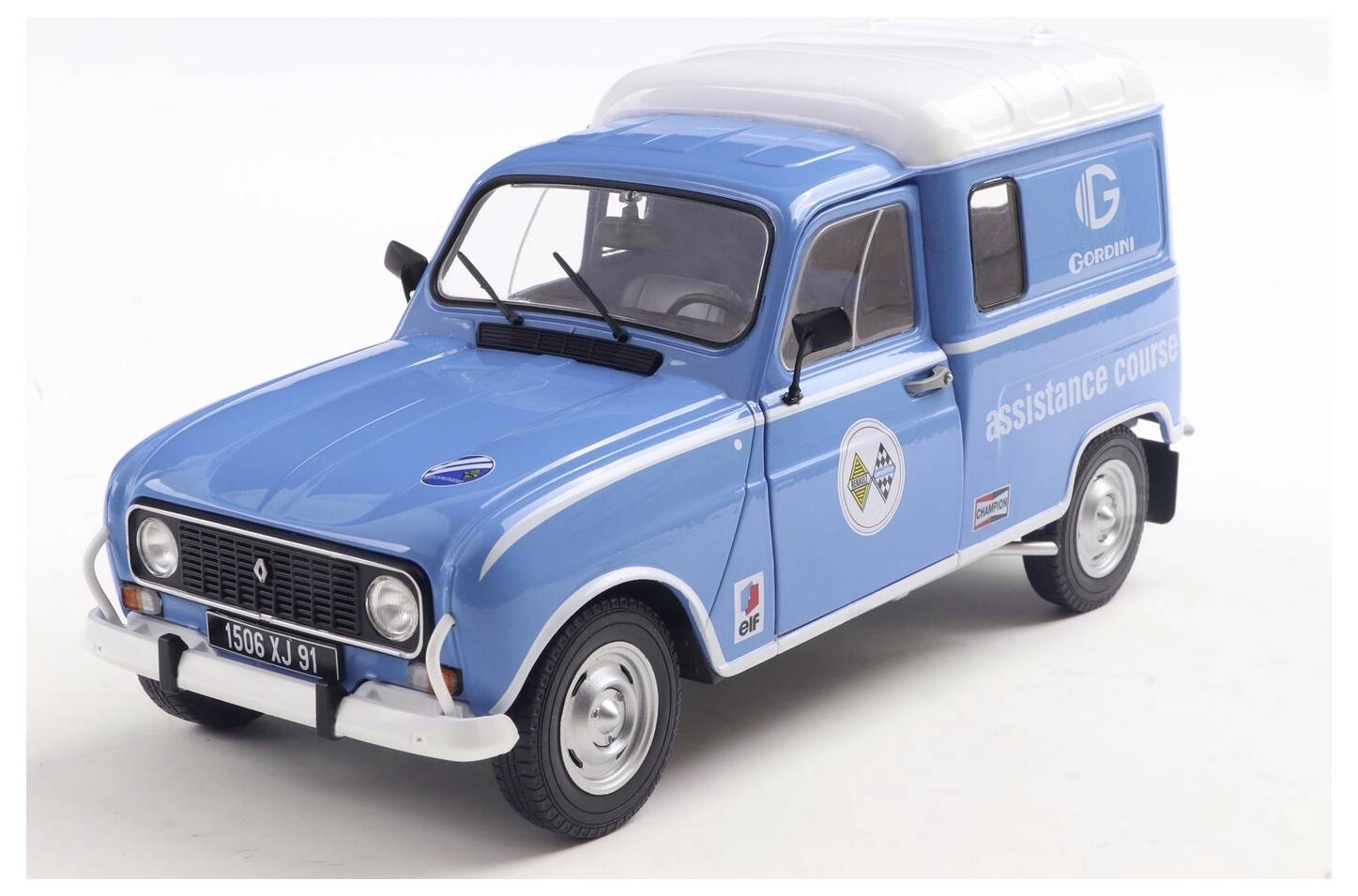 Een vintage blauwe Renault bestelwagen met de tekst 'assistance course' aan de zijkant, voorzien van een bedrijfslogo en rallyplakkers.