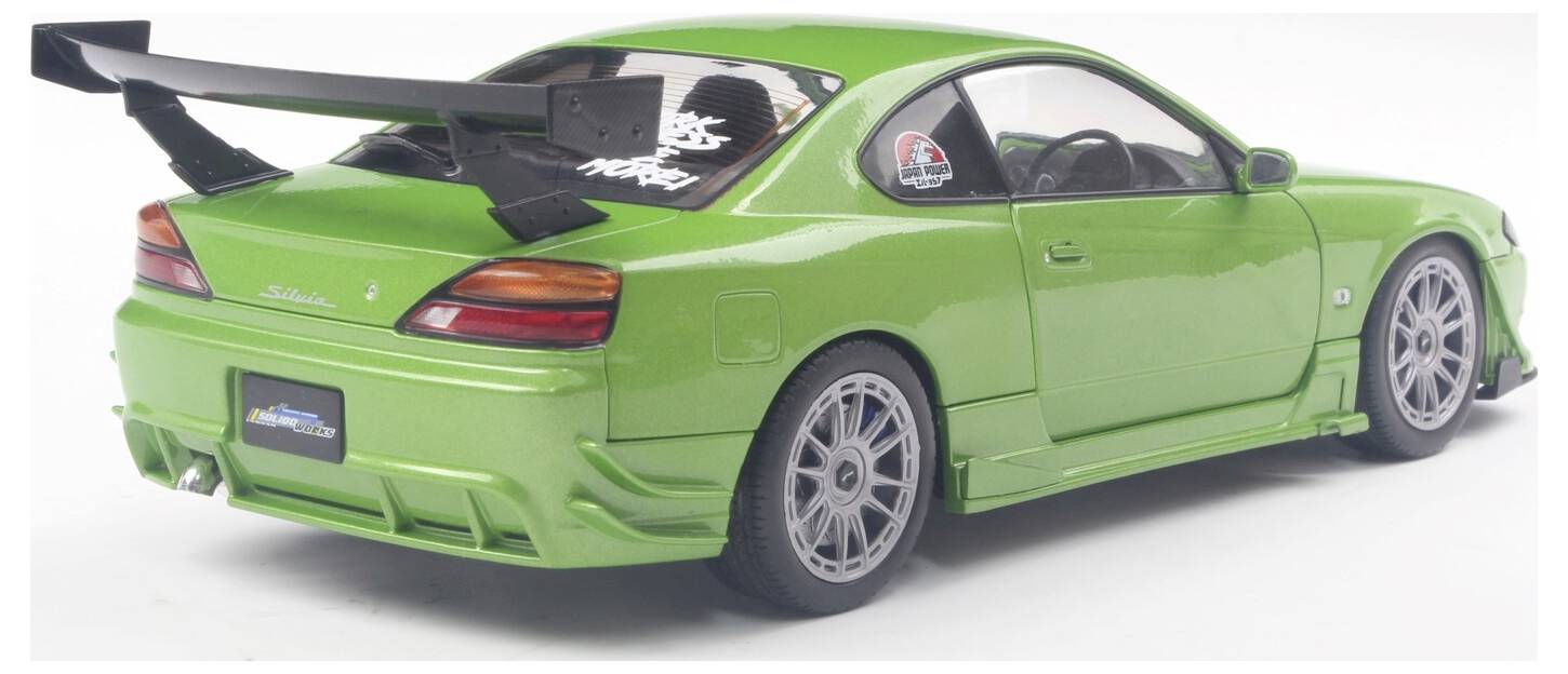 Een groene sportwagen met een grote achterspoiler en aangepaste velgen geparkeerd, bekeken vanuit een achter- en zijaanzicht, waarbij het strakke design wordt getoond.