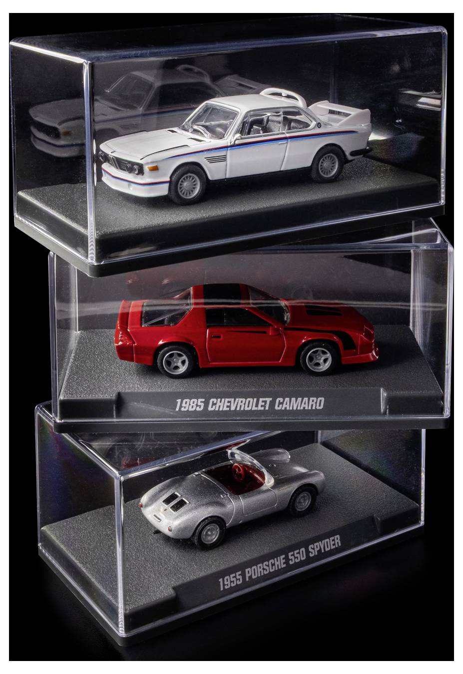 Drie modelauto's in vitrinekasten: een witte sportwagen, een '1985 Chevrolet Camaro' in rood, en een '1955 Porsche 550 Spyder' in wit.