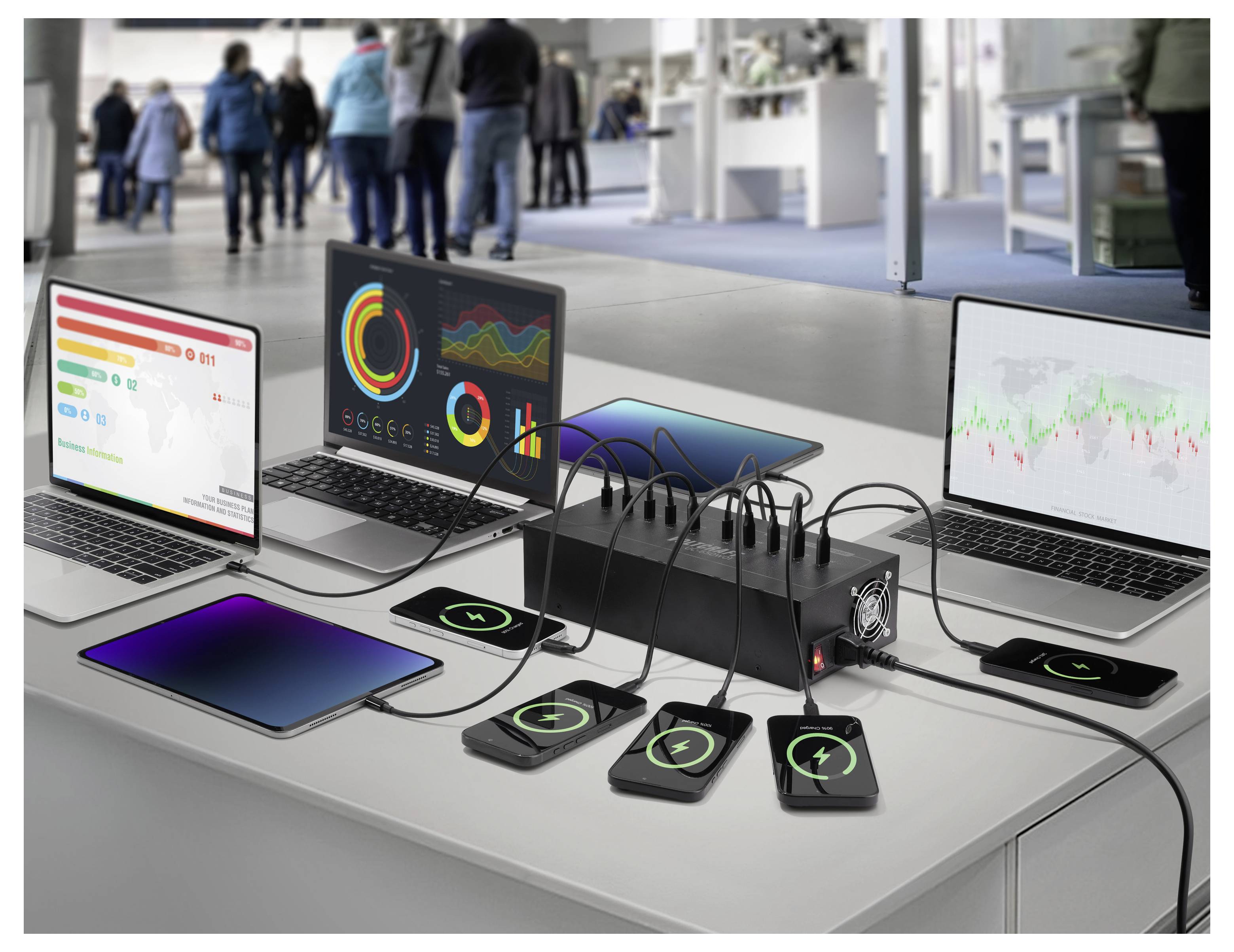 Tafelblad tech display met laptops, tablet, telefoons en een centraal laadstation dat meerdere apparaten oplaadt terwijl het kleurrijke datasdashboards toont.