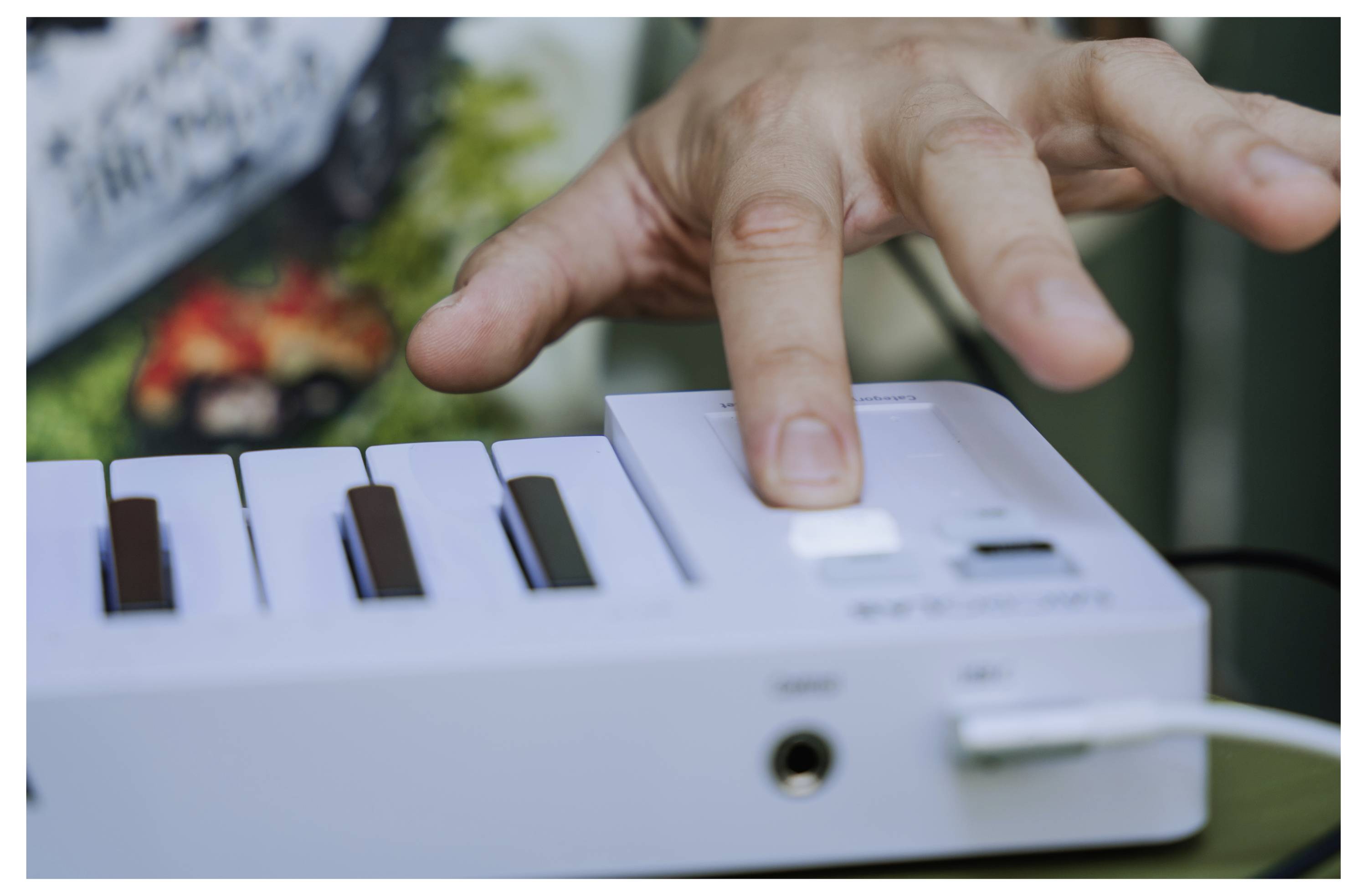 Hand die op een knop drukt op een wit elektronisch muziekinstrument met toetsen, met de focus op interactie en bedieningsfunctie.