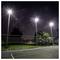 Een tennisbaan 's avonds verlicht door felle bovenverlichting, omringd door een draadgaas hek, met bomen op de achtergrond.