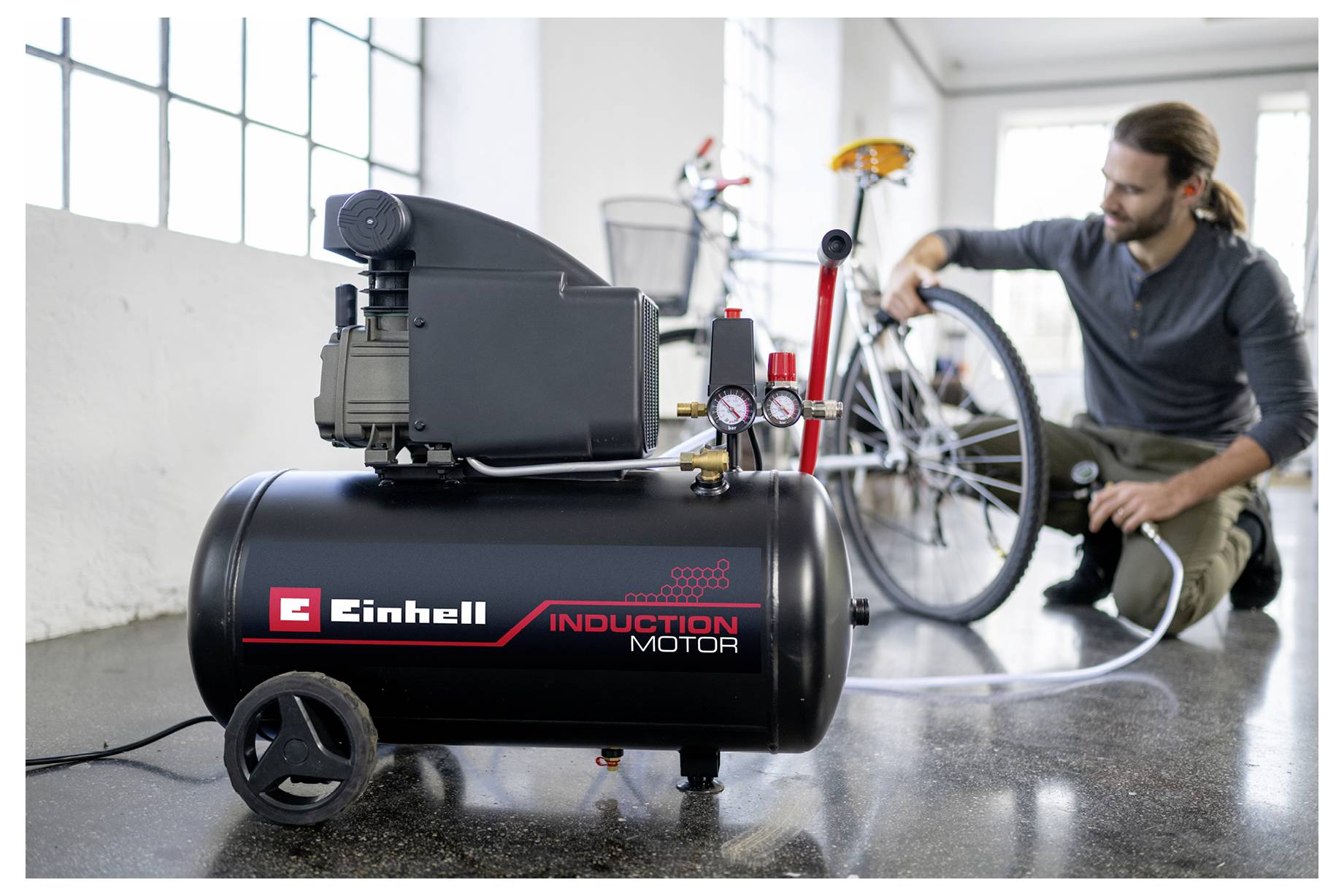 Een persoon pompt een fietstijd op met een luchtcompressor met het label 'Einhell Inductiemotor' in een lichte, ruime ruimte.