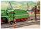 Een modelspoorbaan diorama toont een groene stoomlocomotief op sporen met arbeiders in de nabijheid en kranen op de achtergrond.